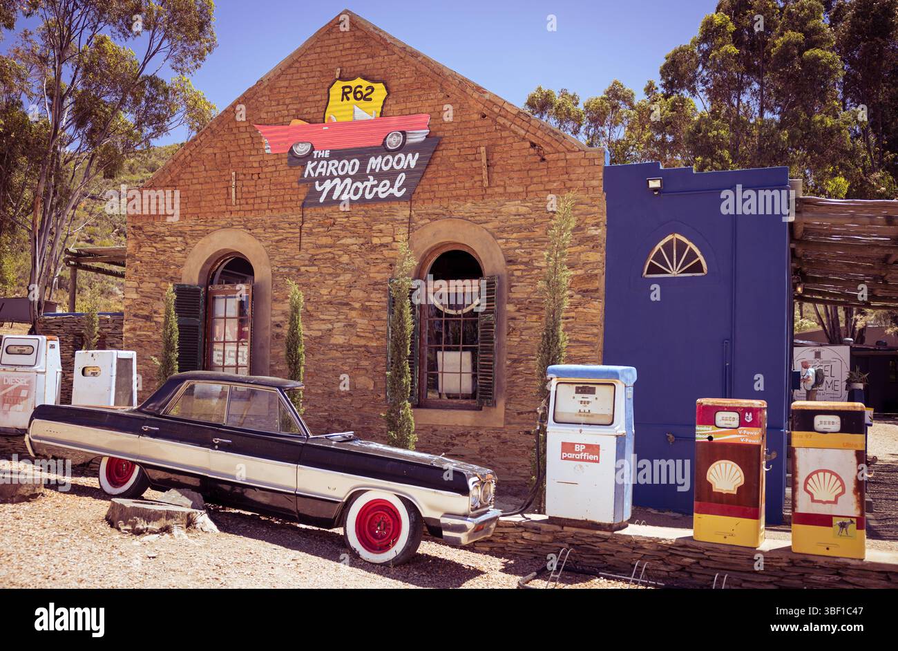 Une voiture classique et des pompes à essence vintage colorées se trouvent à l'extérieur du Karoo Moon Motel sur la route 62 en Afrique du Sud, entourées de panneaux rétro et de chars rustiques Banque D'Images