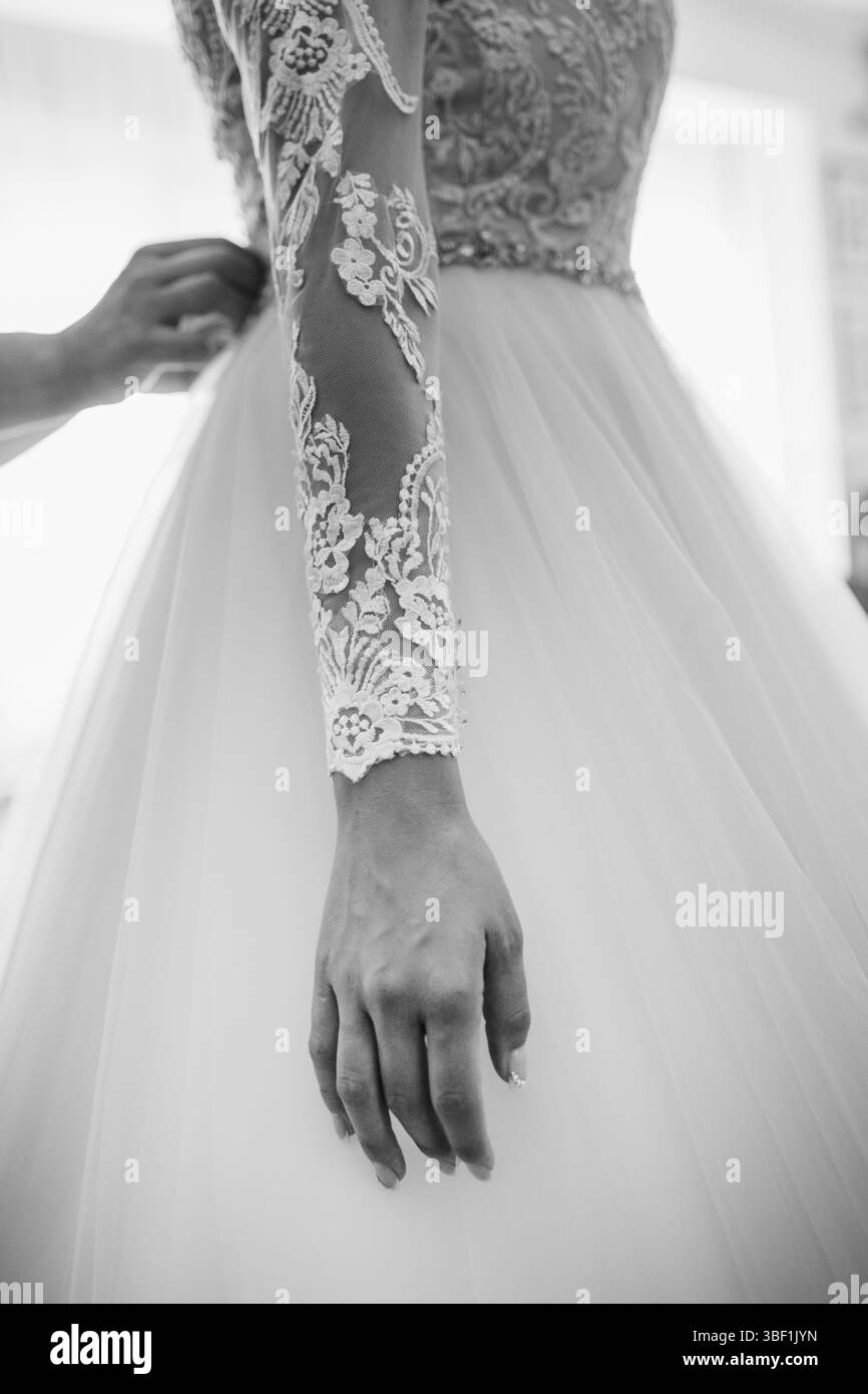 Une mariée ajuste une robe de mariée, mettant en valeur des détails de dentelle complexes et un tissu délicat, soulignant les préparations méticuleuses et l'anticipation befo Banque D'Images