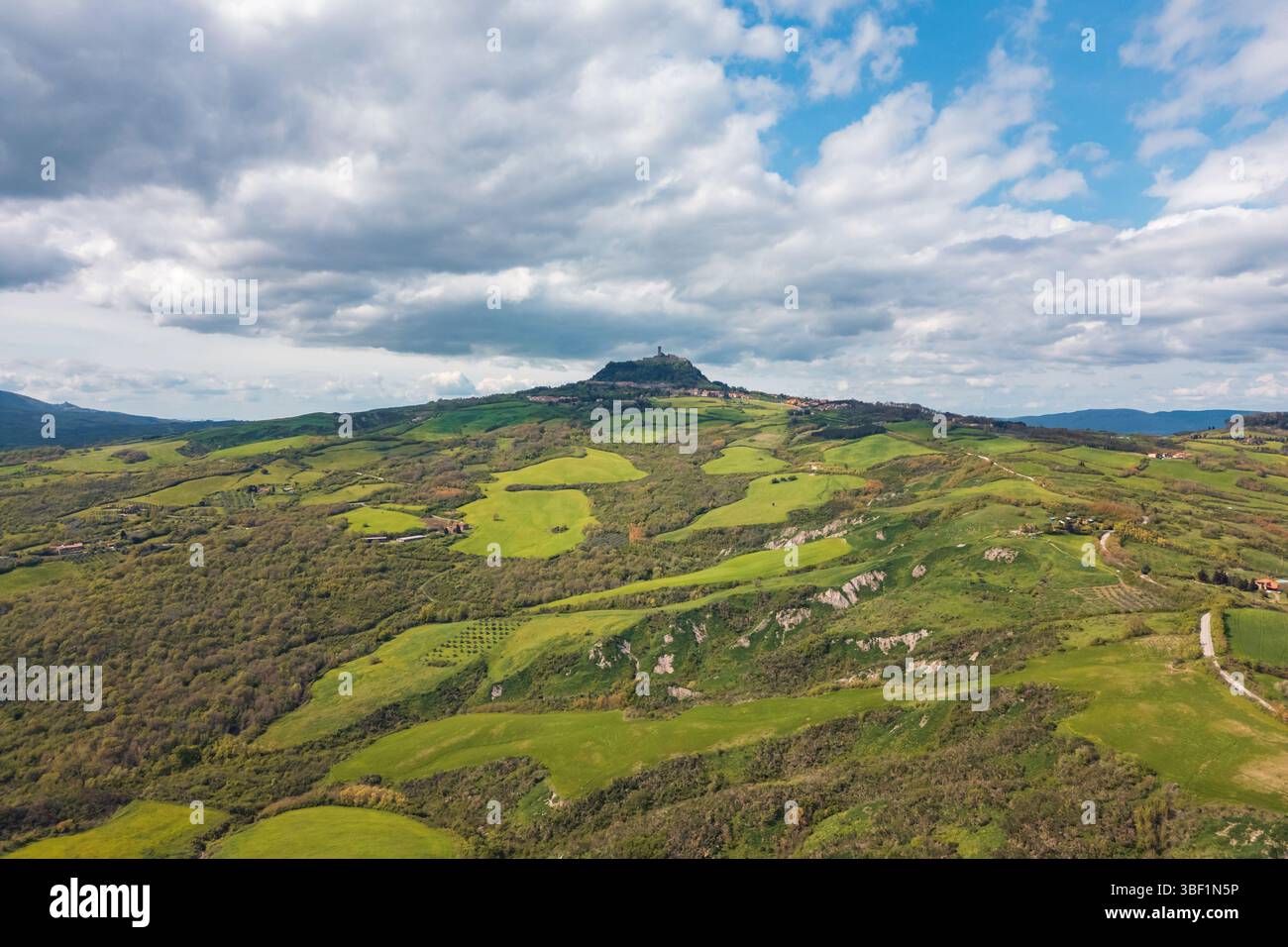 Vue imprenable sur les collines vallonnées de Toscane sous un ciel nuageux. Des champs verdoyants et une ville historique perchée créent un paysage pittoresque, idéal Banque D'Images