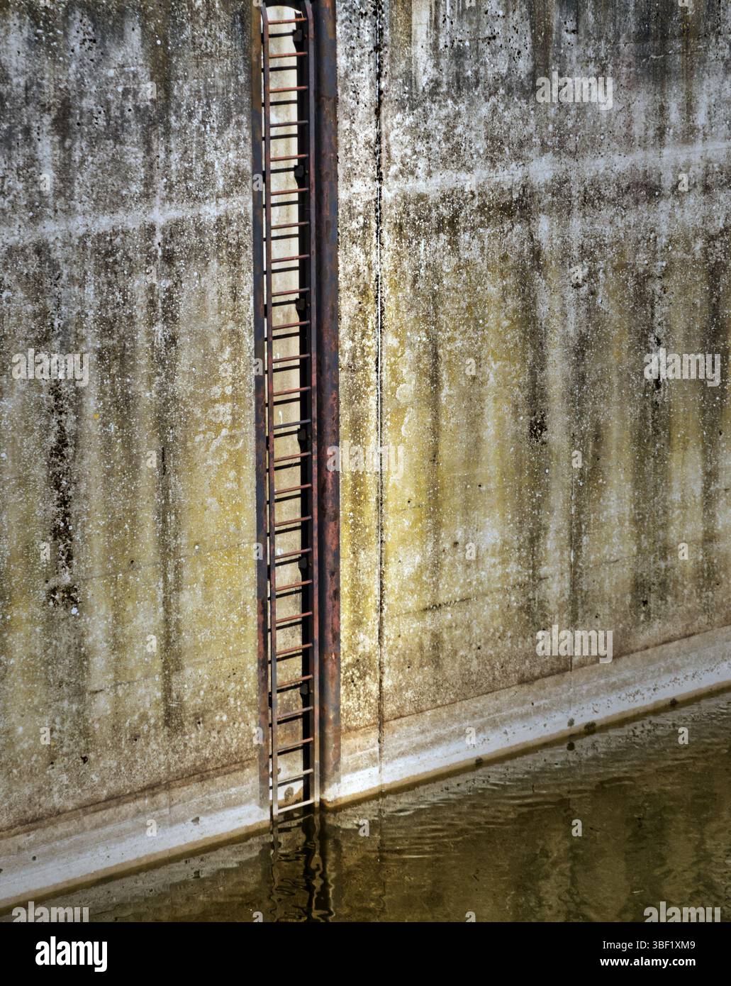 Echelle de secours en métal rouillé partiellement immergée dans l'eau calme, attachée à un mur de béton altéré, fournissant l'accès et la sécurité dans l'industrie ou wa Banque D'Images