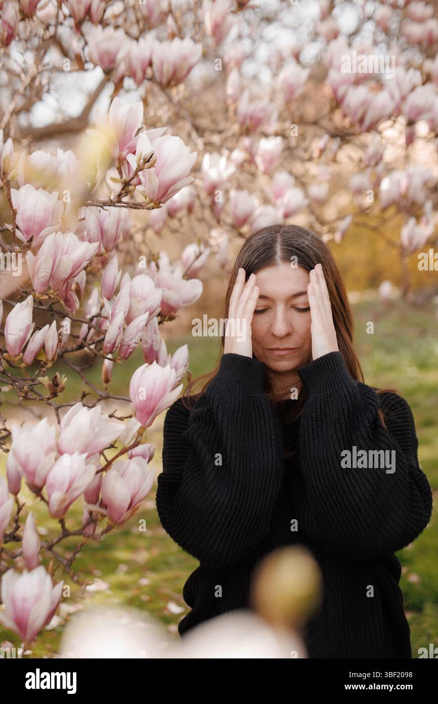 Jeune femme souffrant de maux de tête près d'un arbre magnolia en fleurs Banque D'Images