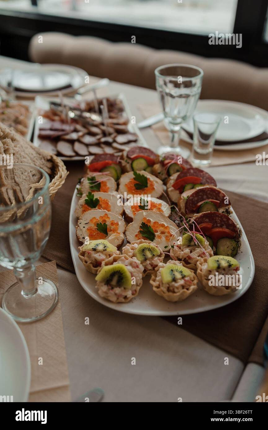 Un gros plan d'une table magnifiquement agencée avec un long plateau chargé de viandes variées, fromages, brochettes de légumes et pâtisseries fourrées, comple Banque D'Images