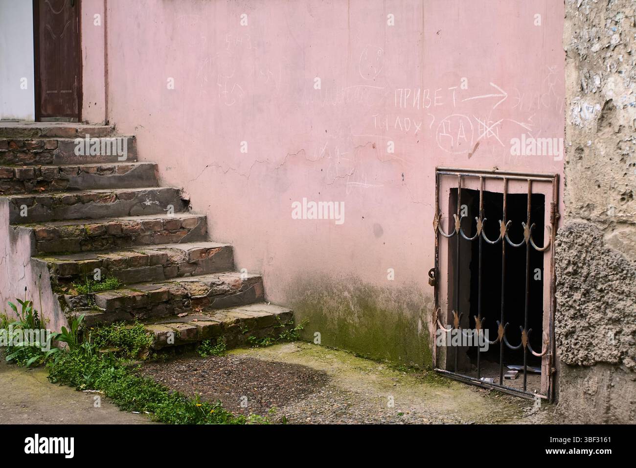 Un fragment d'un ancien bâtiment avec un escalier en pierre menant vers le haut et une fenêtre barrée en dessous. Murs minables, verdure Banque D'Images