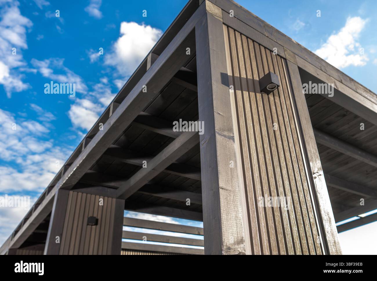 Un pavillon contemporain se dresse haut avec des lattes en bois sur fond de ciel bleu et de nuages moelleux, mettant en valeur son design élégant et sa respiration parfaite Banque D'Images