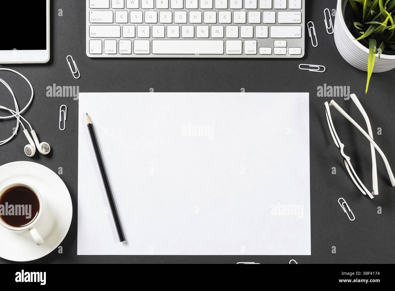 Vue de dessus du lieu de travail moderne avec feuille de papier vierge. Surface noire plate avec smartphone, bloc-notes et tasse de café. Vue de dessus de l'espace de travail de bureau et Banque D'Images