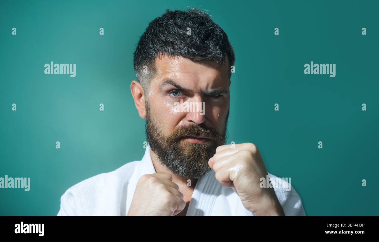 Karaté homme en posture de combat. Le combattant masculin de karaté pratique des coups de poing pendant l'entraînement de karaté. Homme barbu en kimono blanc avec les mains serrées dans le poing R Banque D'Images