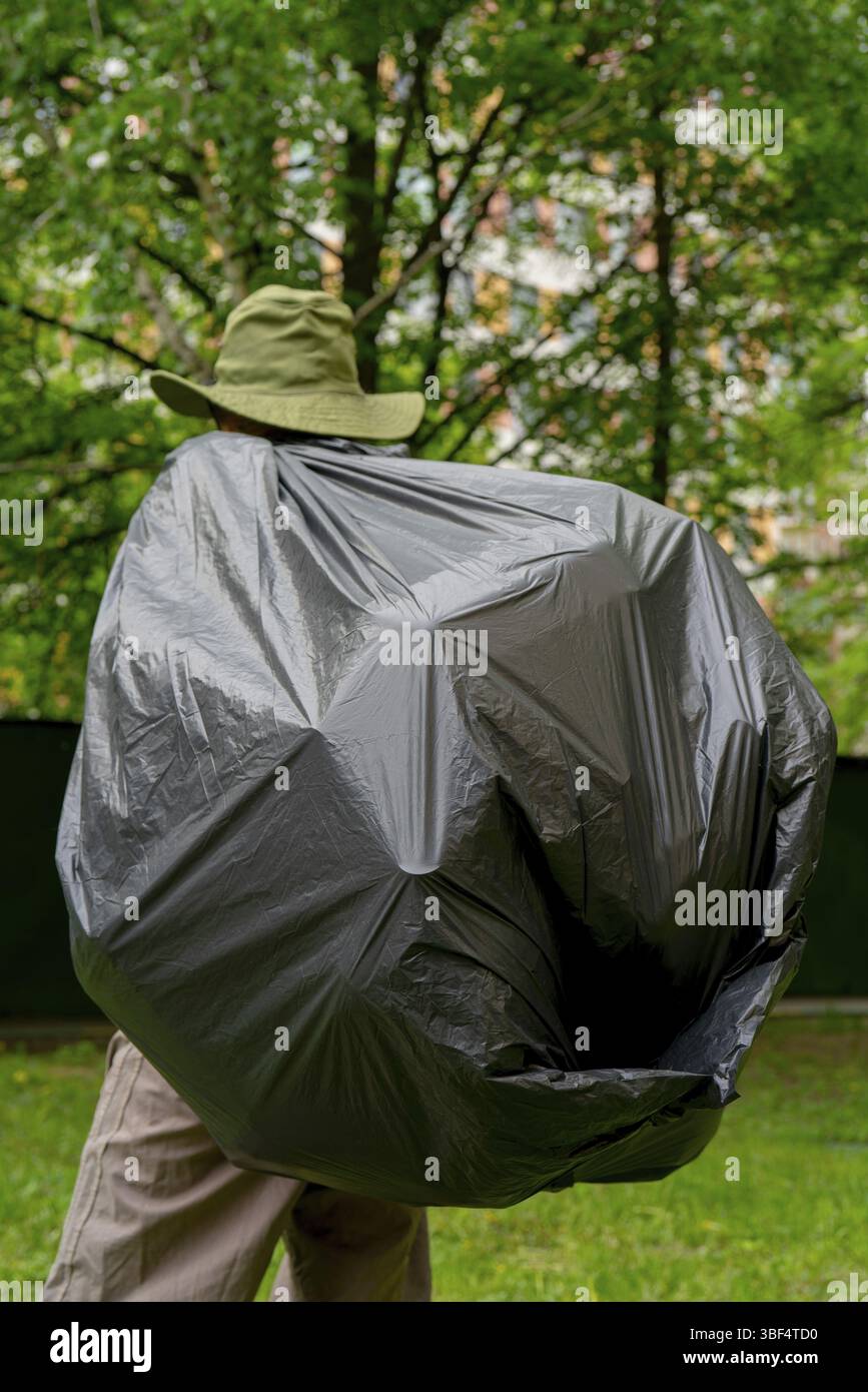 Récupération des ordures. L'homme porte un grand sac poubelle noir Banque D'Images