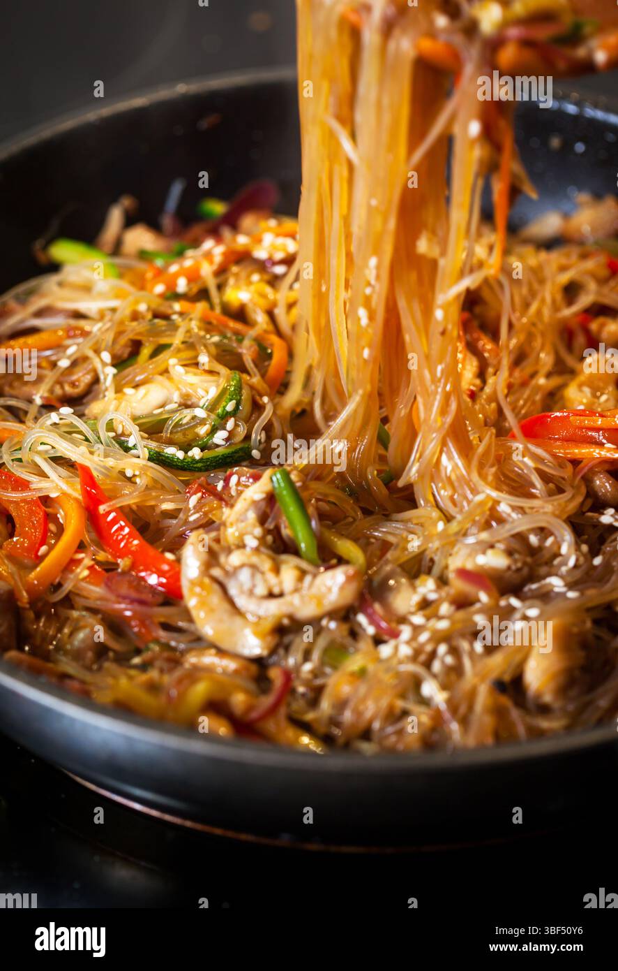 Nouilles asiatiques en verre sauter avec du poulet et des légumes dans une poêle Banque D'Images