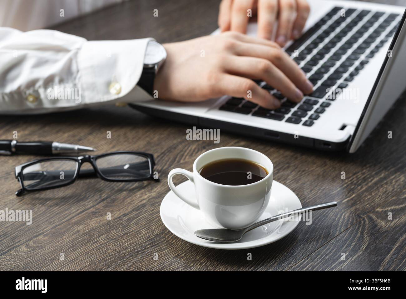 Homme d'affaires assis au bureau et utilisant un ordinateur portable. Gros plan sur les mains de l'homme tapant sur le clavier au bureau. Espace de consultation avec vue latérale avec lunettes et Banque D'Images