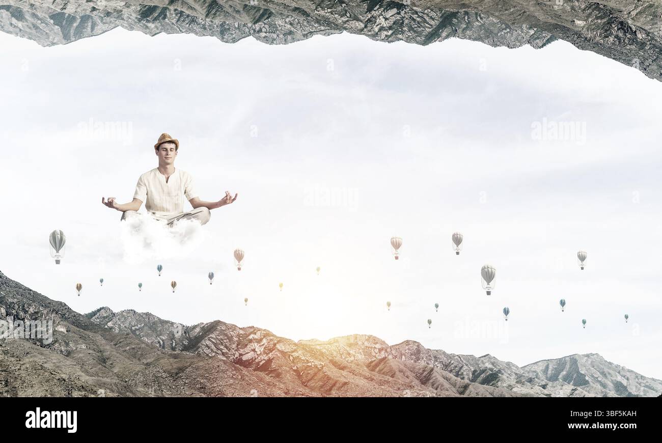 Jeune homme gardant les yeux fermés et regardant concentré tout en méditant sur les nuages parmi les aérostats volants et entre deux mondes de la nature Banque D'Images