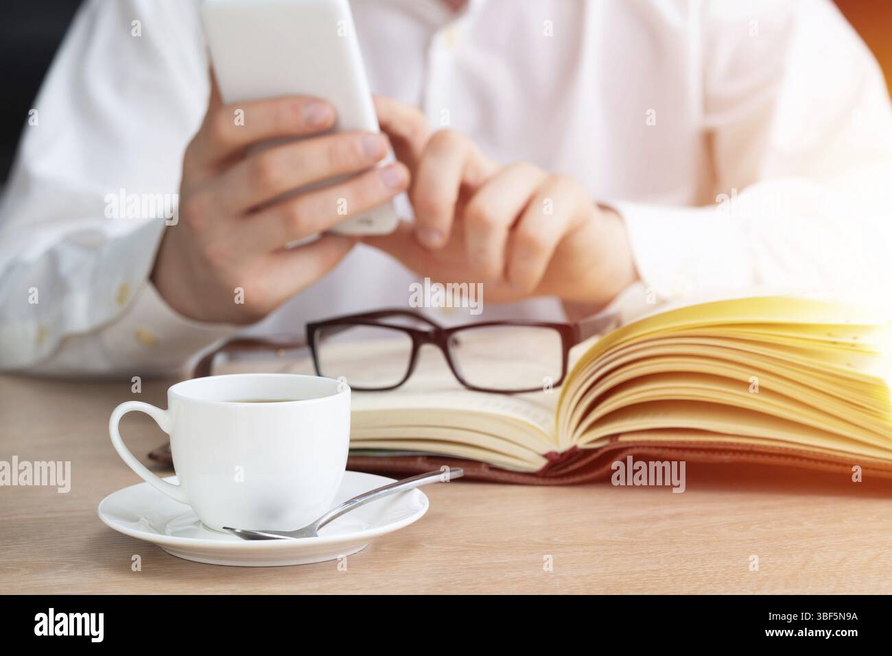 Homme en chemise blanche à l'aide d'un smartphone comme assis au bureau avec une tasse de café. Application professionnelle et technologie mobile. Navigation Internet et communication Banque D'Images
