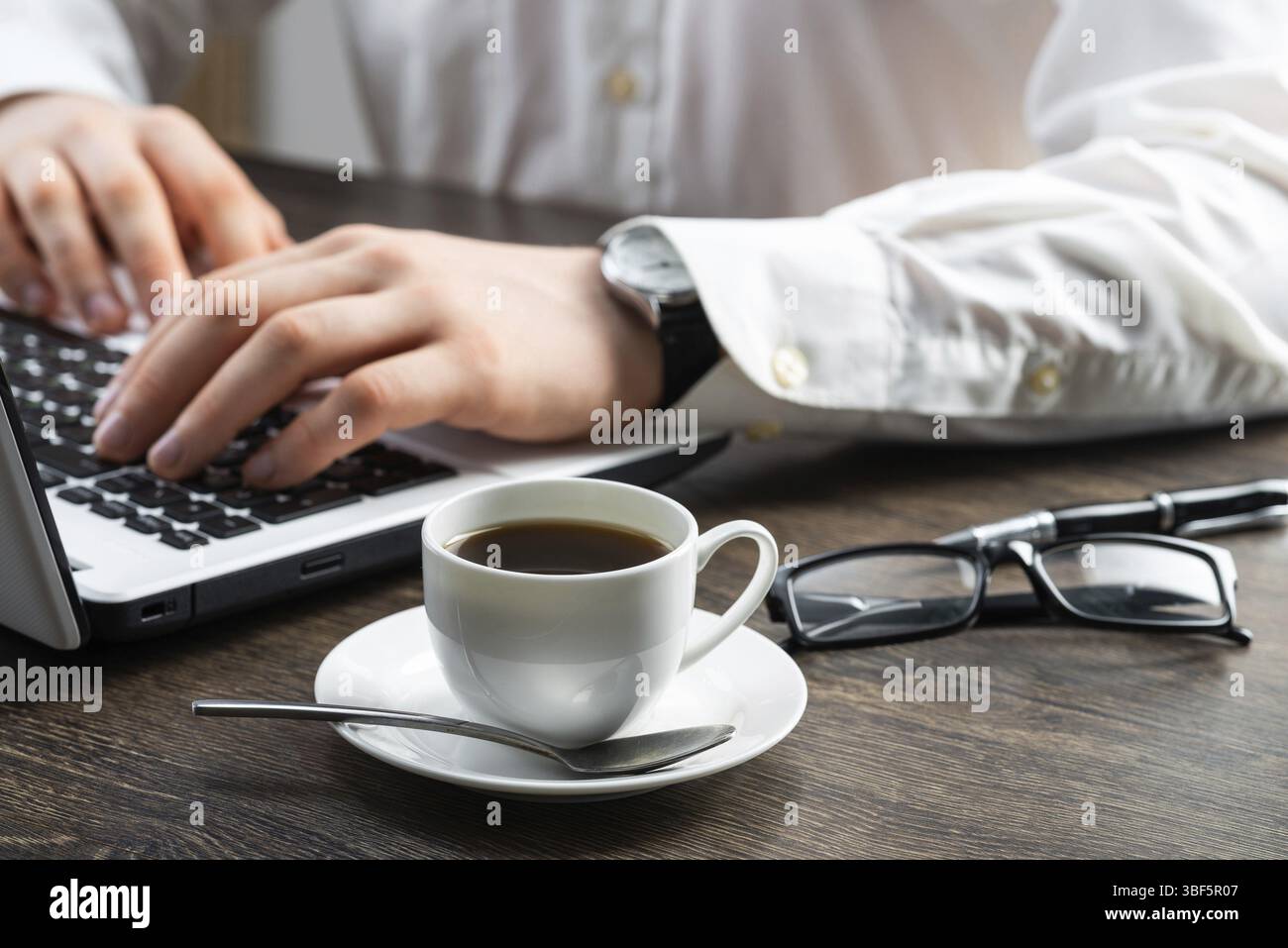 Homme d'affaires assis au bureau et travaillant avec un ordinateur portable. Gros plan des mains de l'homme tapant sur le clavier dans le bureau. Lieu de travail d'homme d'affaires avec des lunettes a Banque D'Images