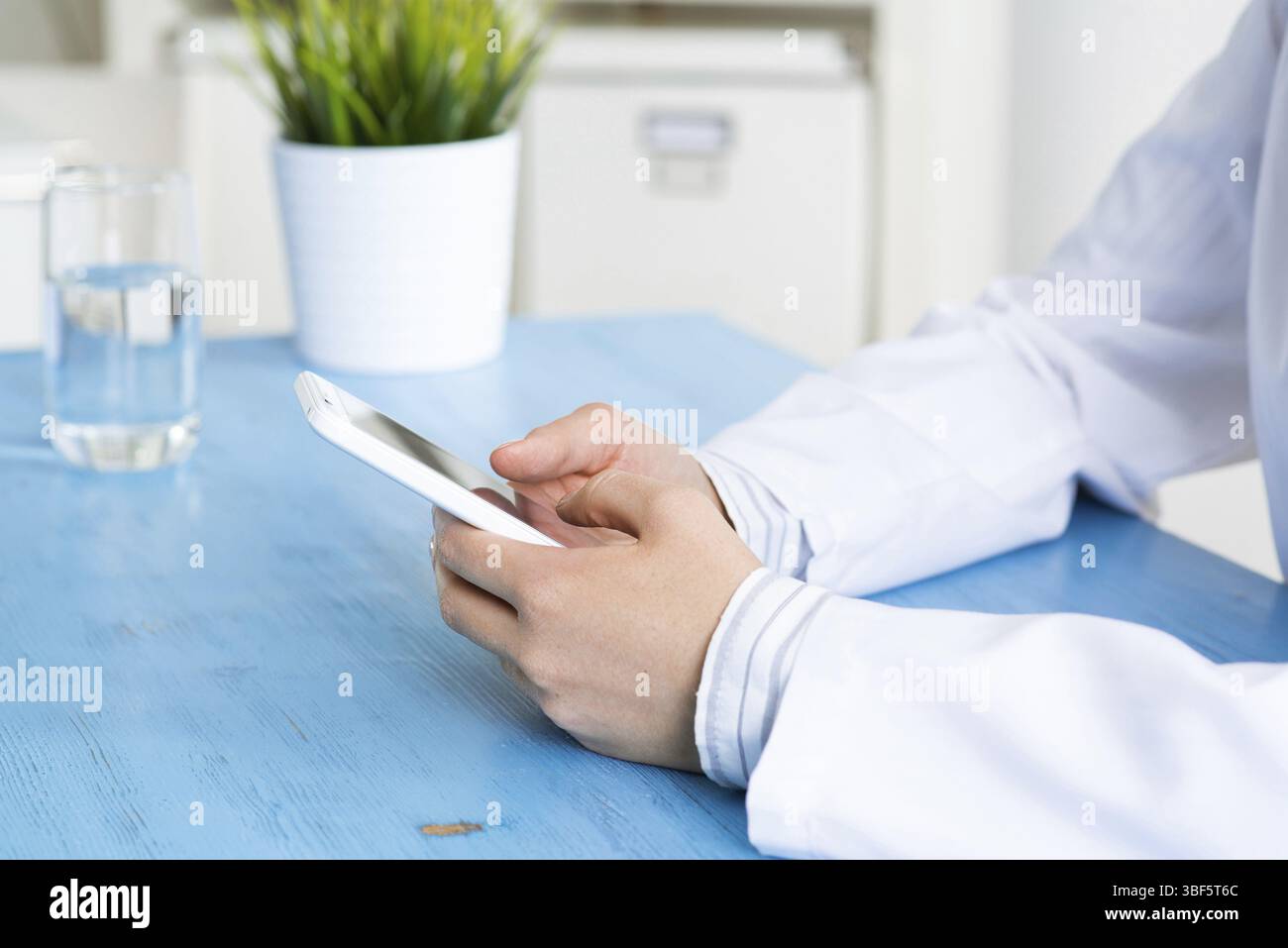 Gros plan des mains du médecin tenant le téléphone portable. Thérapeute en blouse médicale blanche message dans le bureau au bureau. Diagnostic professionnel et traitement en HO Banque D'Images