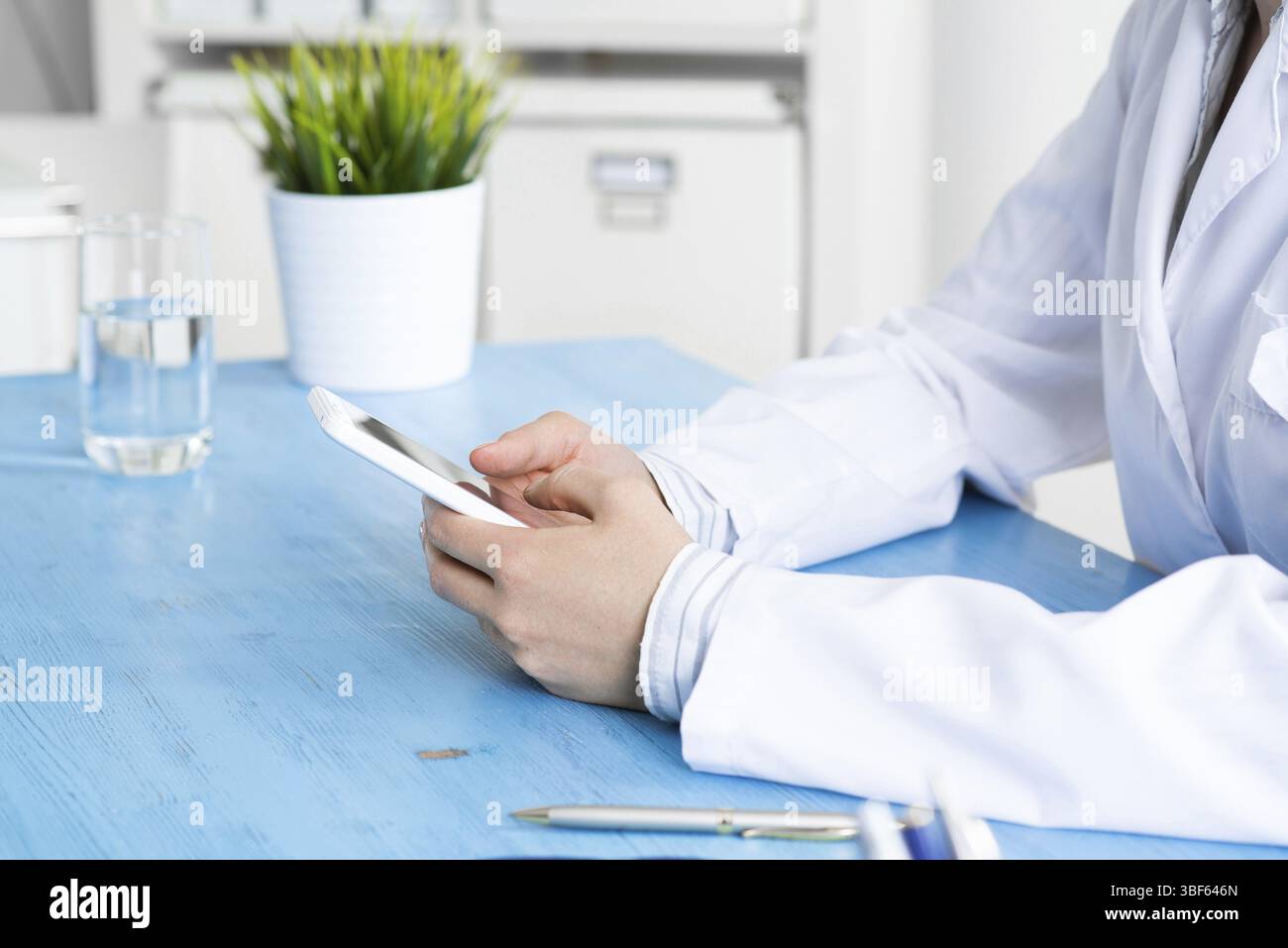 Gros plan des mains du médecin tenant le téléphone portable. Thérapeute en blouse médicale blanche message dans le bureau au bureau. Diagnostic professionnel et traitement en HO Banque D'Images