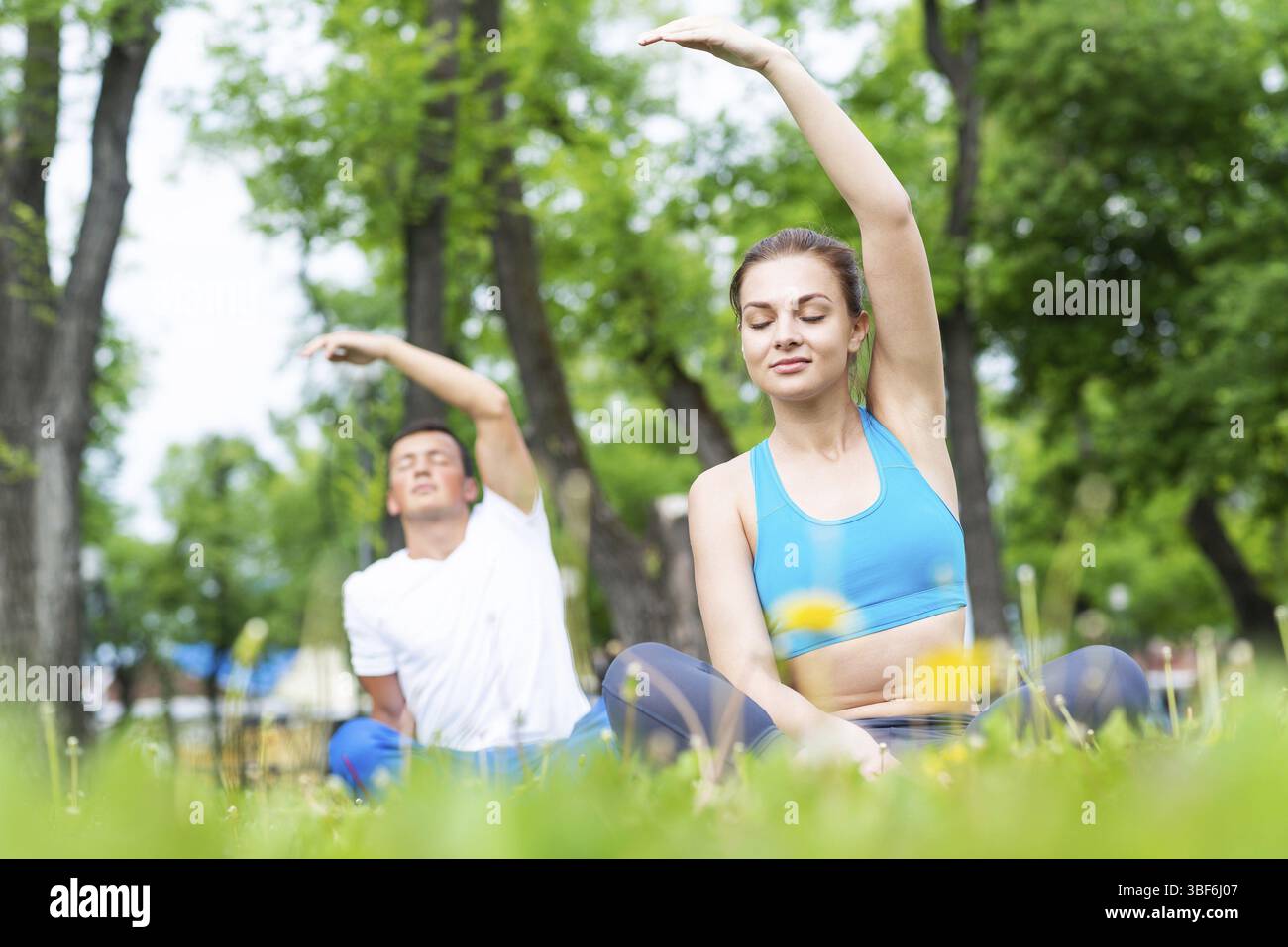Jeune couple faisant du yoga dans le parc ensemble. Homme et femme assis dans le yoga pose sur l'herbe verte. Entraînement et méditation en cours de yoga en plein air au su ensoleillé Banque D'Images
