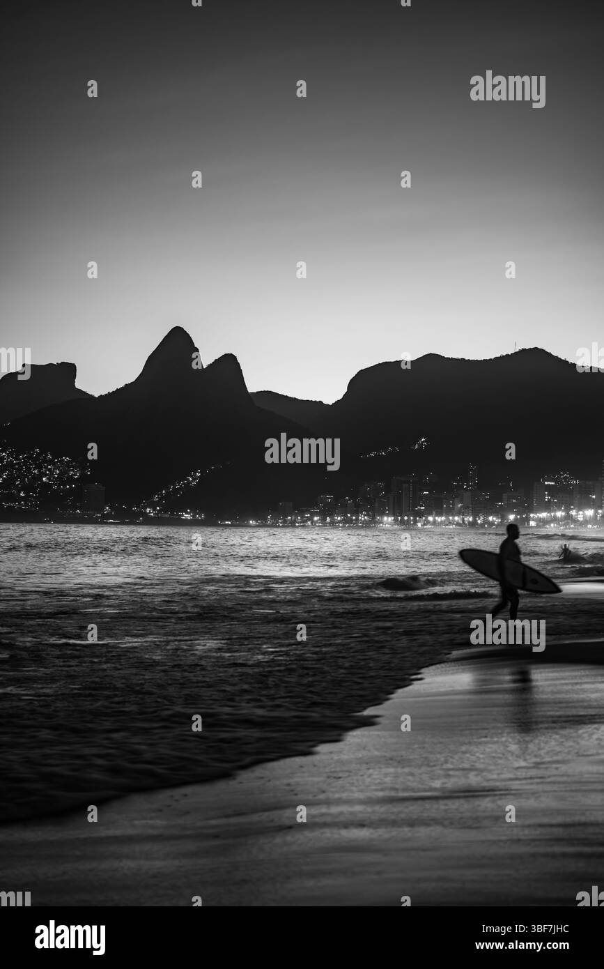 Plage d'Ipanema en Monochrome avec surfeur marchant hors de la mer et Morro dois Irmãos en arrière-plan - Rio de Janeiro, Brésil Banque D'Images