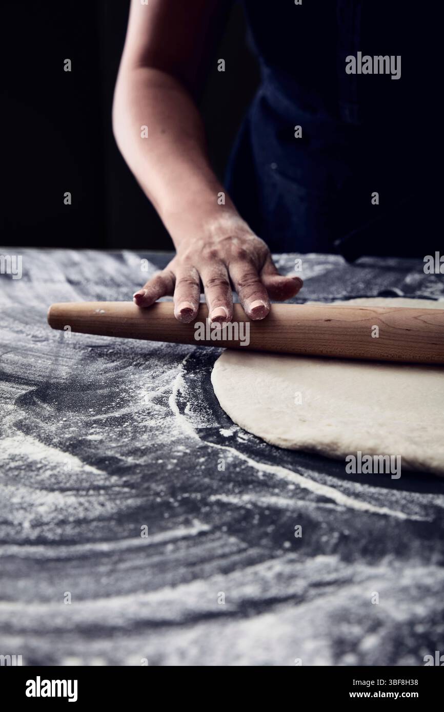 Pâte à rouler à la main avec une broche en bois sur un comptoir recouvert de farine Banque D'Images