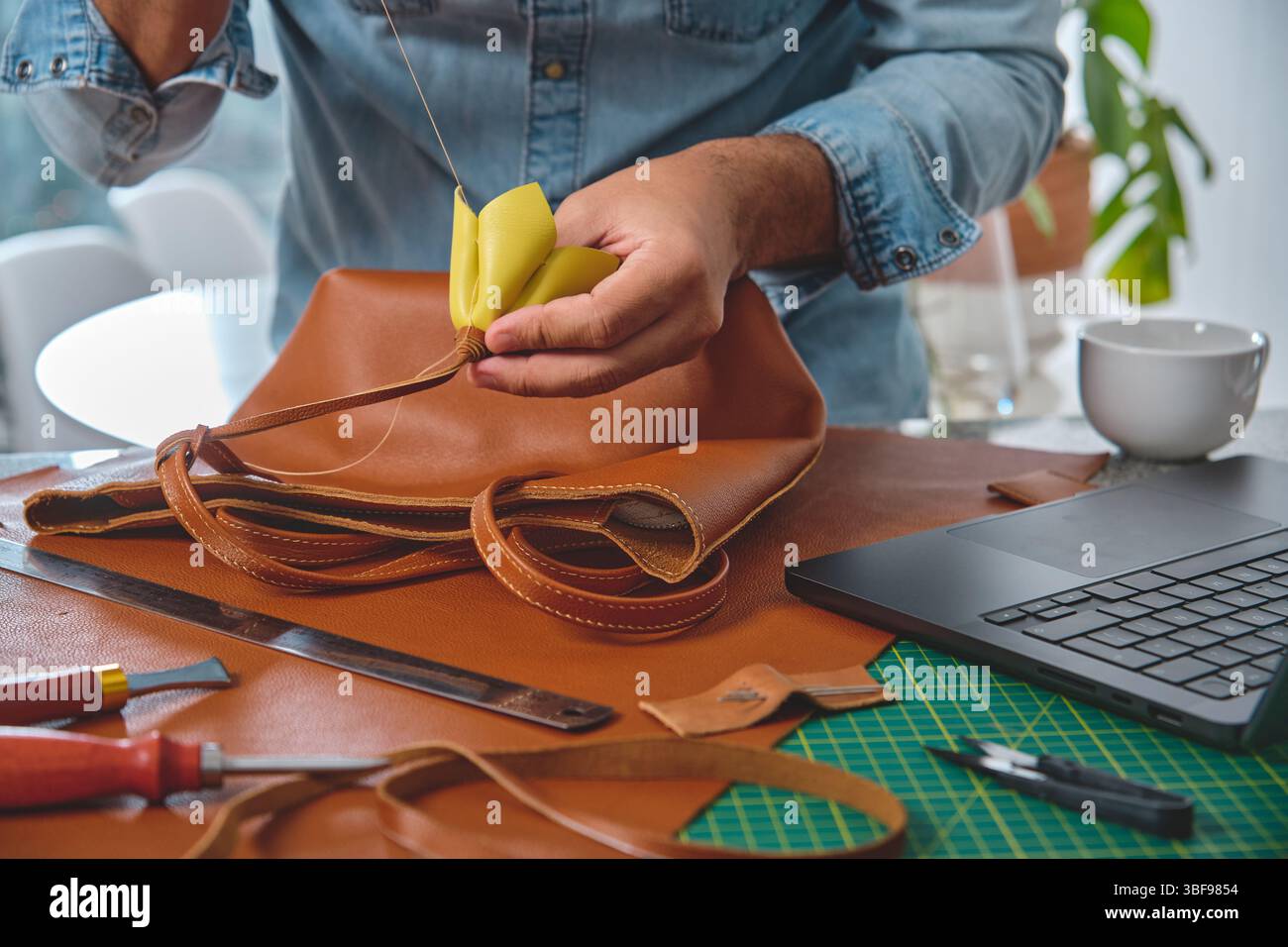 L’artisan cuir coud une poignée de sac dans son atelier, en utilisant des techniques traditionnelles et des matériaux de haute qualité Banque D'Images