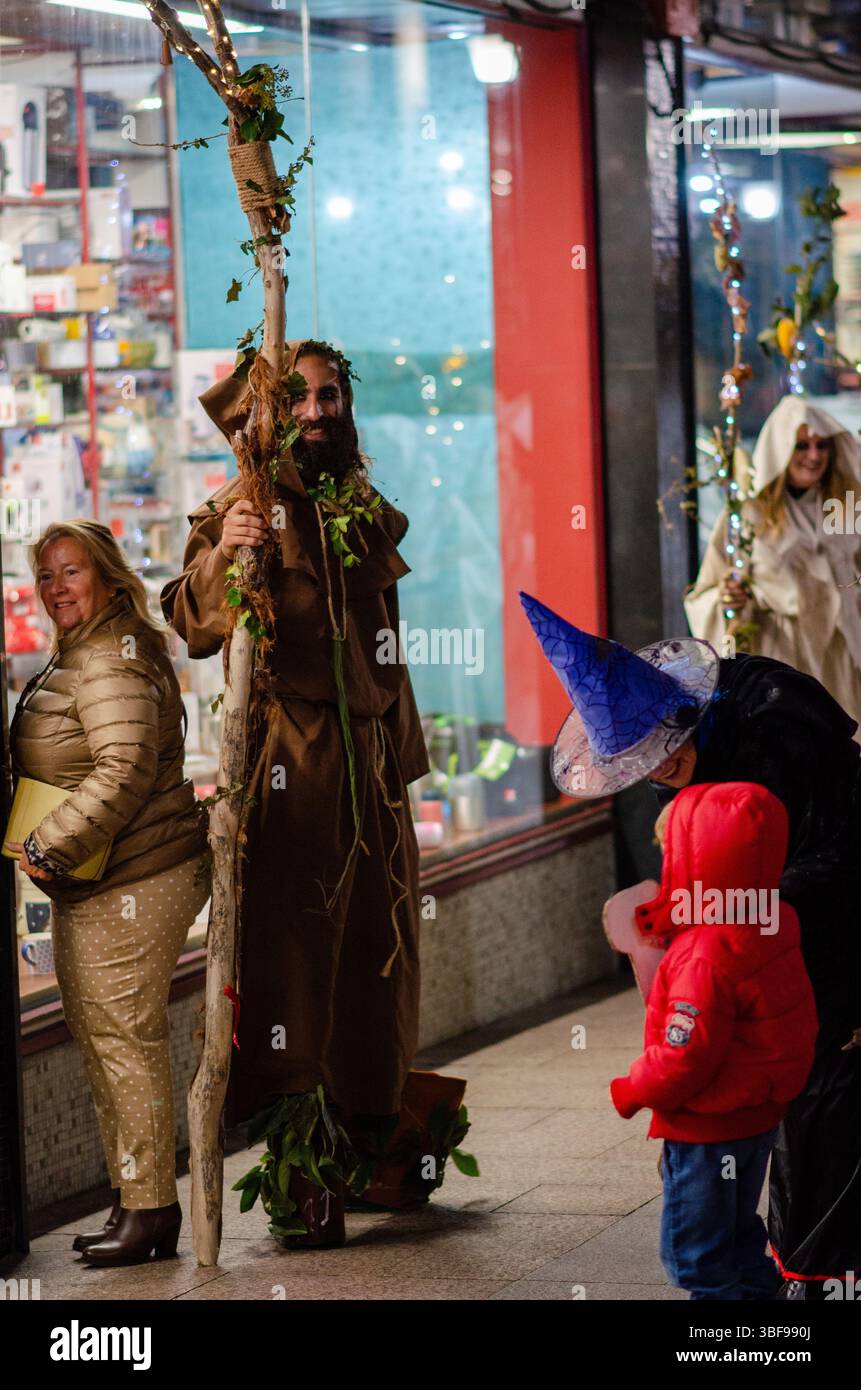 Scène de rue atmosphérique en soirée lors d'un carnaval espagnol d'Halloween, mettant en vedette des adultes et des enfants en costumes fantastiques pour profiter de célébrations festives. Banque D'Images