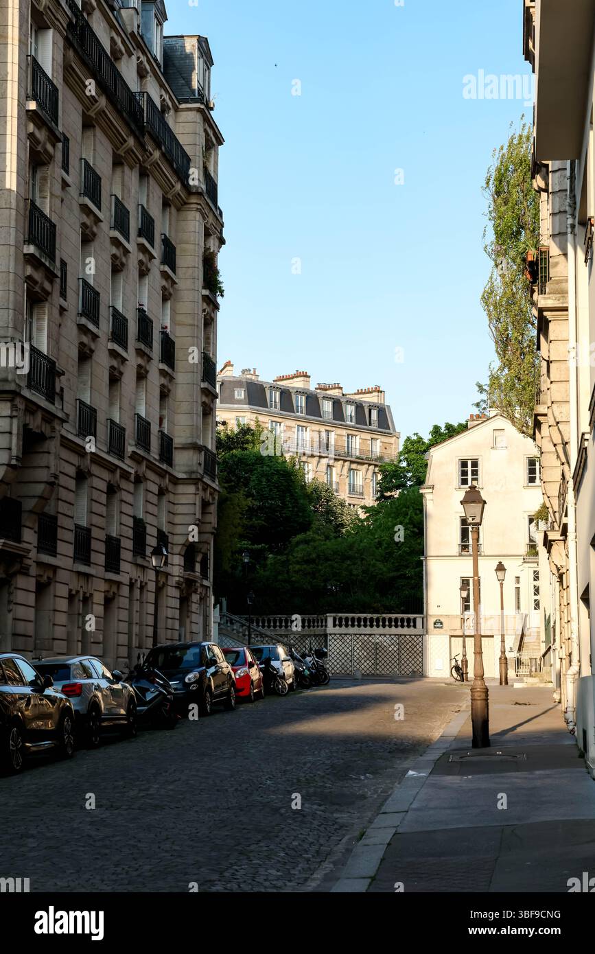 Une vue sur une rue parisienne calme et étroite pavée de pavés, bordée d'immeubles d'habitation traditionnels et de voitures garées, Banque D'Images