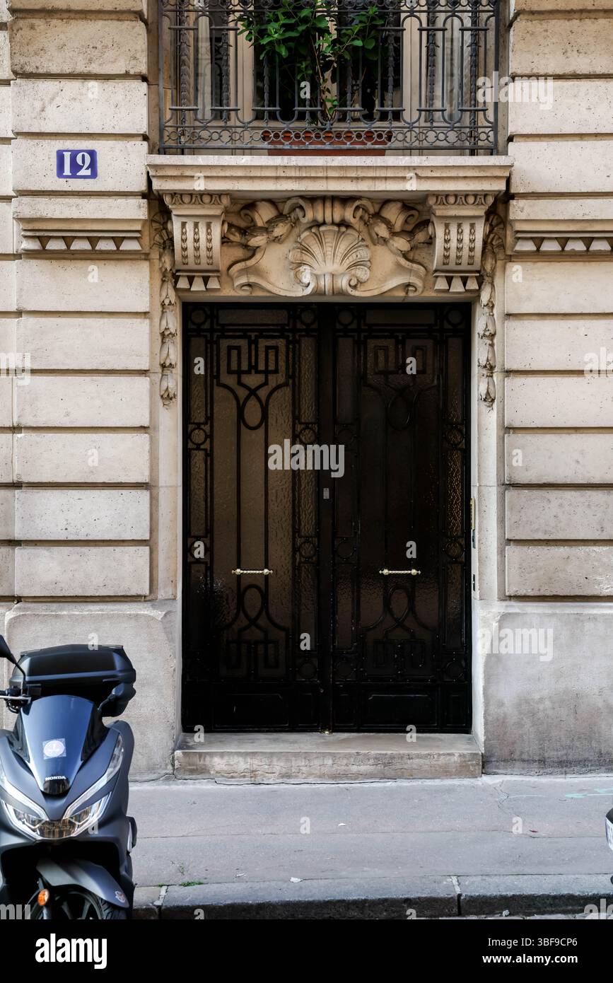 L'entrée d'un bâtiment parisien avec une porte double noire élégante et ornée dans un cadre en pierre sculptée, avec le numéro de maison 12 au-dessus et Banque D'Images