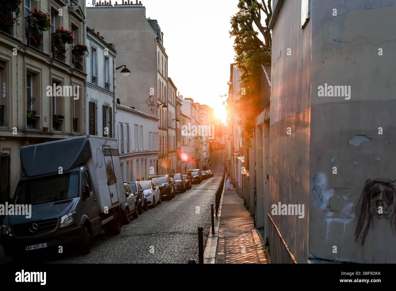 Une vue imprenable sur une étroite rue pavée parisienne, éclairée de façon spectaculaire par l'intense lumière dorée du soleil couchant, projetant de longues ombres A. Banque D'Images