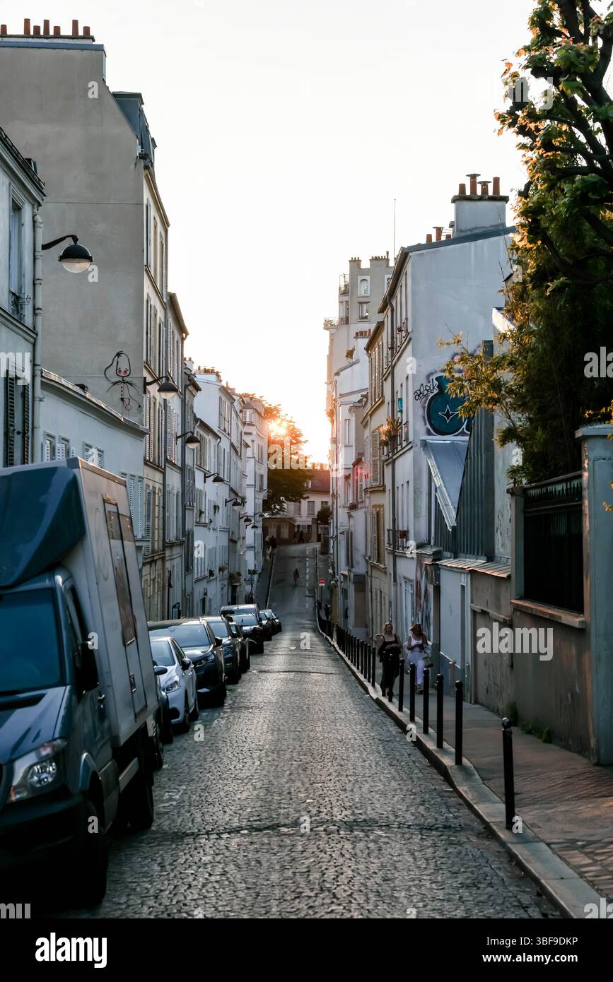 Une vue imprenable sur une étroite rue pavée parisienne, éclairée de façon spectaculaire par l'intense lumière dorée du soleil couchant, projetant de longues ombres A. Banque D'Images