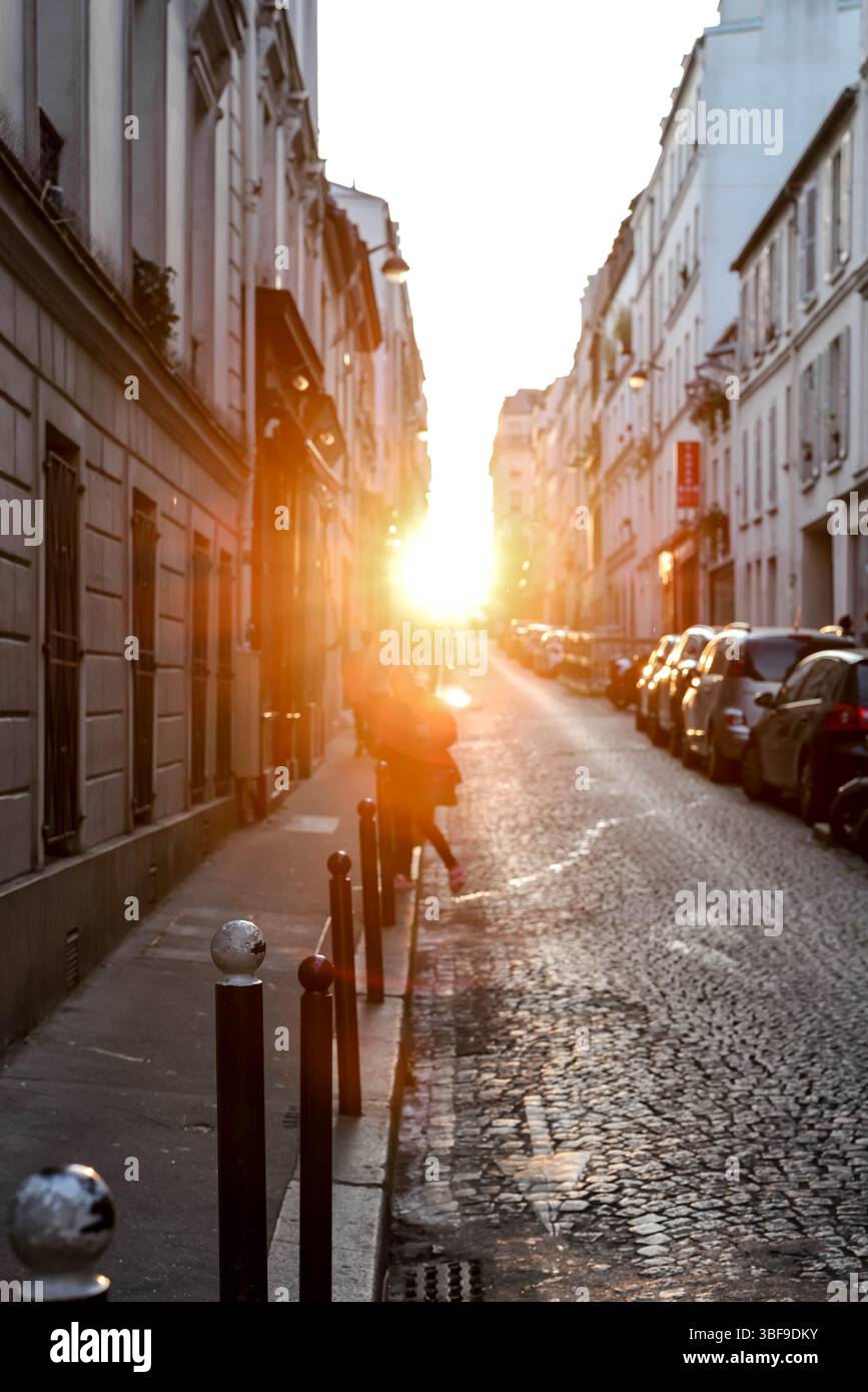Une vue imprenable sur une étroite rue pavée parisienne, éclairée de façon spectaculaire par l'intense lumière dorée du soleil couchant, projetant de longues ombres A. Banque D'Images