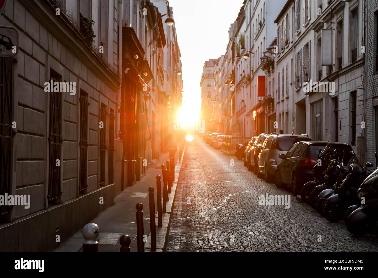 Une vue imprenable sur une étroite rue pavée parisienne, éclairée de façon spectaculaire par l'intense lumière dorée du soleil couchant, projetant de longues ombres A. Banque D'Images