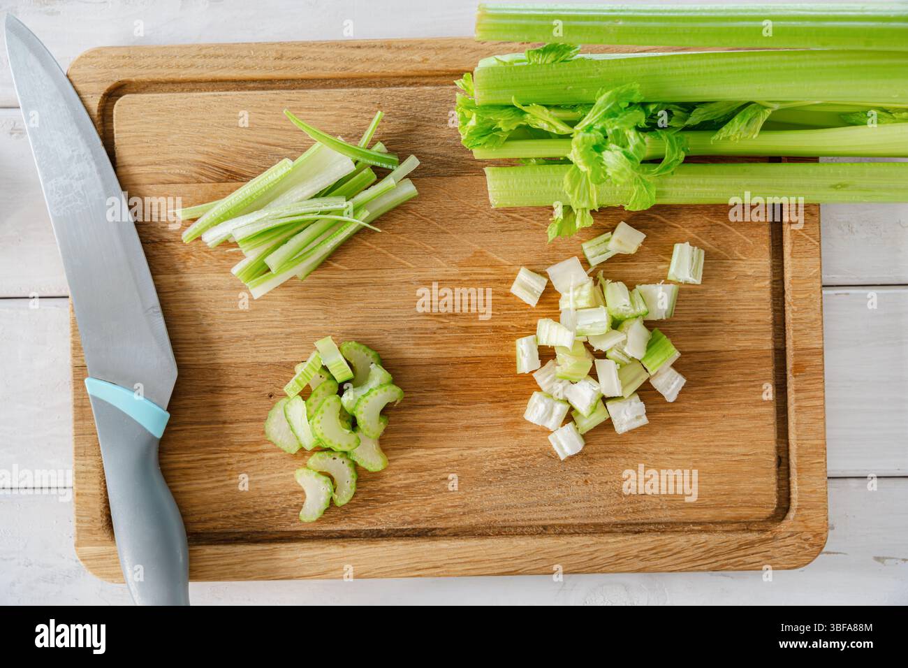 Branches de céleri tranchées de plusieurs façons avec un couteau de cuisine sur une planche de bois pour la préparation des repas. Cuisine saine Banque D'Images