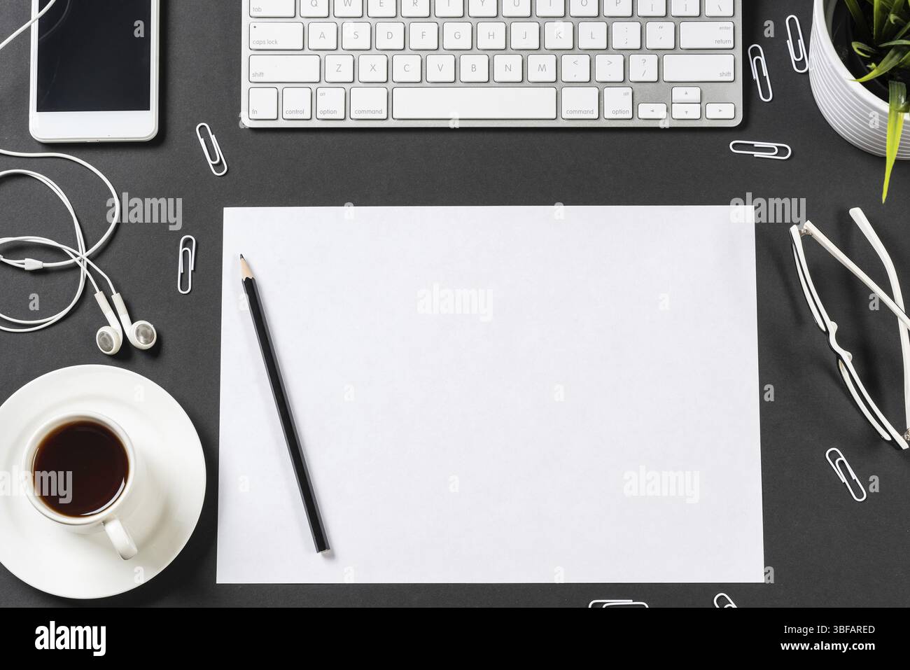 Vue de dessus du lieu de travail moderne avec feuille de papier vierge. Surface noire plate avec smartphone, bloc-notes et tasse de café. Vue de dessus de l'espace de travail de bureau et Banque D'Images