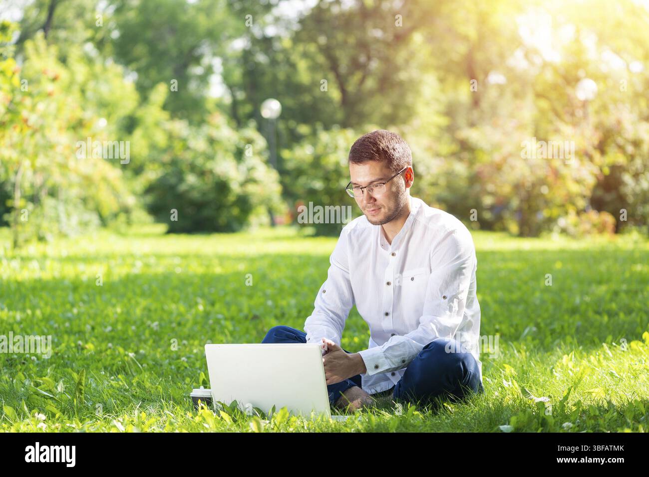 Young businessman using laptop computer on Green grass in park. Bel homme dans les vêtements de travail avec l'extérieur à l'ordinateur journée ensoleillée. Freela Banque D'Images