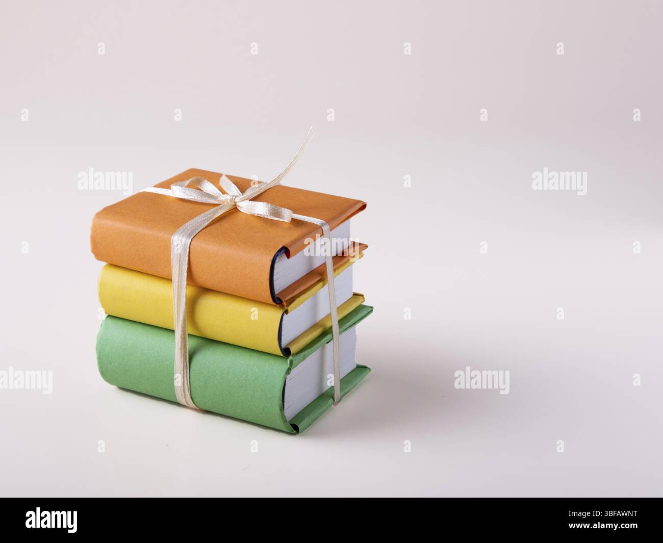 Une pile de mini livres en couvertures lumineuses nouées avec un ruban de satin, sur un fond blanc, espace pour le texte Banque D'Images
