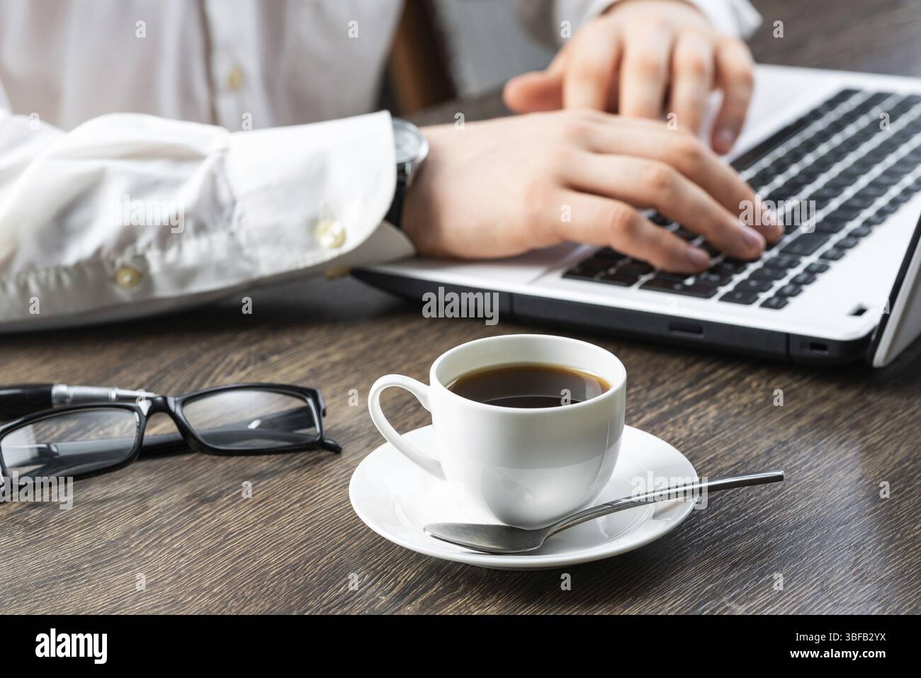 Homme d'affaires assis au bureau et utilisant un ordinateur portable. Gros plan sur les mains de l'homme tapant sur le clavier au bureau. Espace de consultation avec vue latérale avec lunettes et Banque D'Images