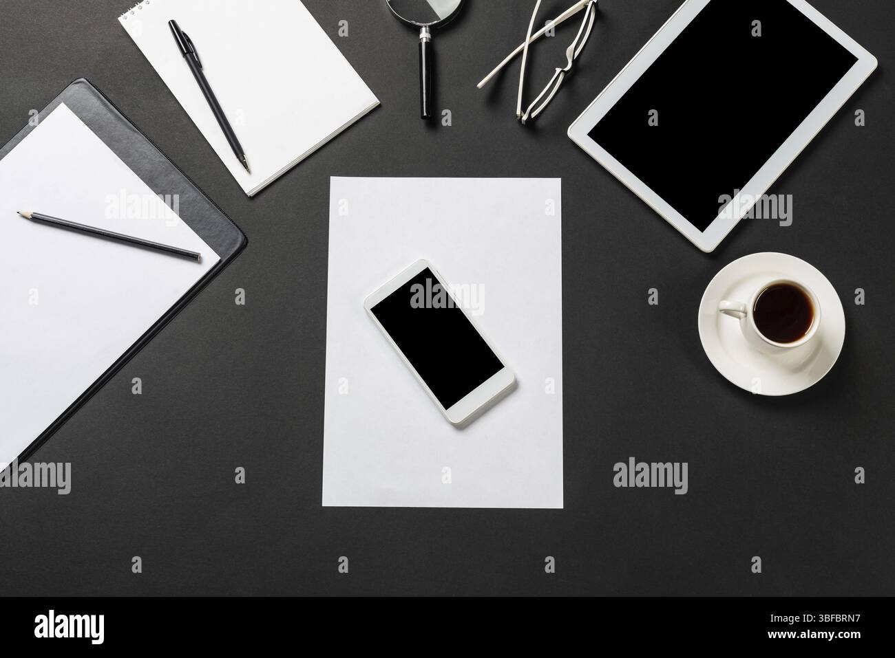 Vue de dessus du lieu de travail moderne avec feuille de papier vierge. Surface noire plate avec smartphone, bloc-notes et tasse de café. Vue de dessus de l'espace de travail de bureau et Banque D'Images
