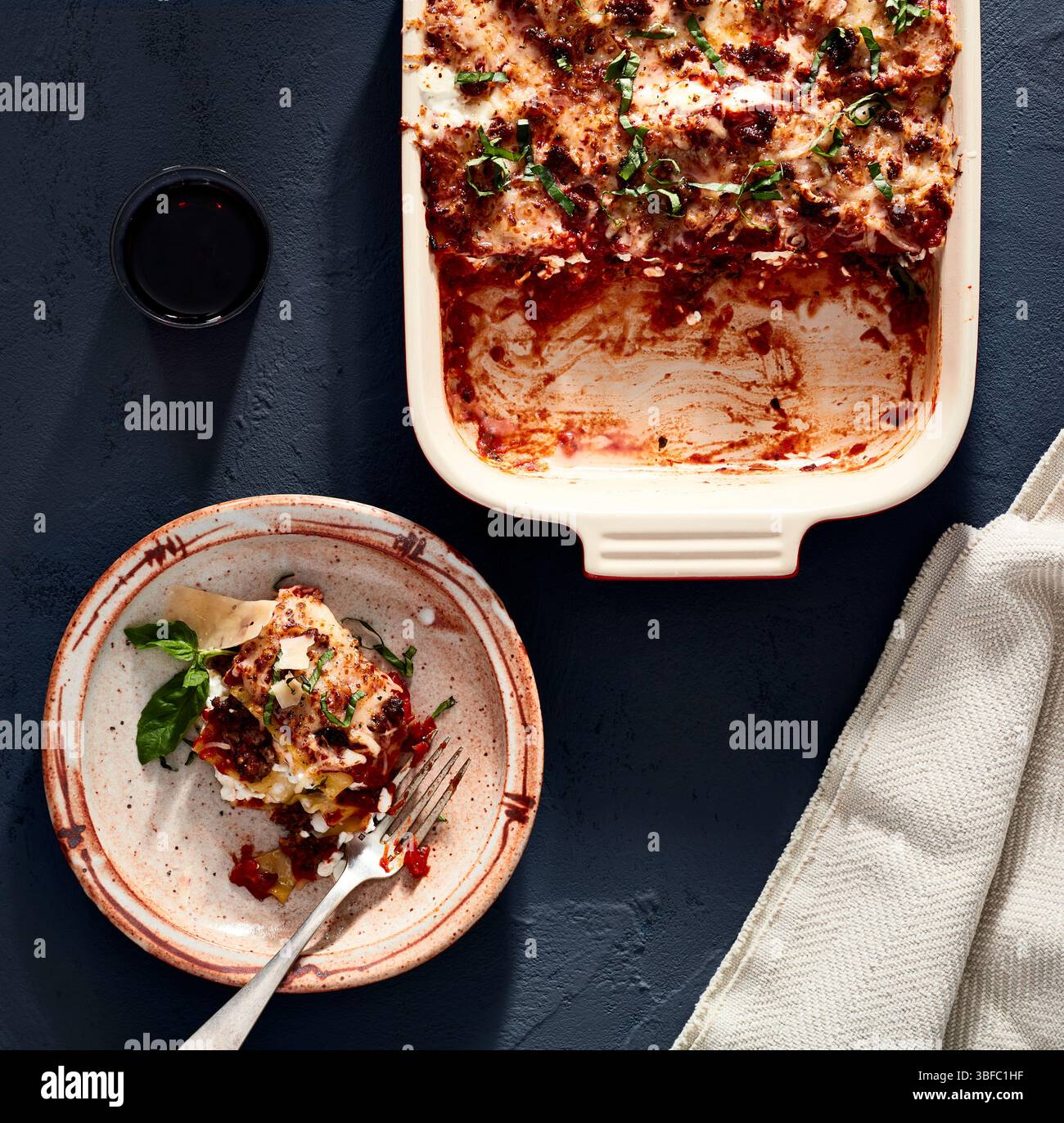 Lasagnes partiellement servies dans un plat avec une tranche plaquée et du vin rouge Banque D'Images