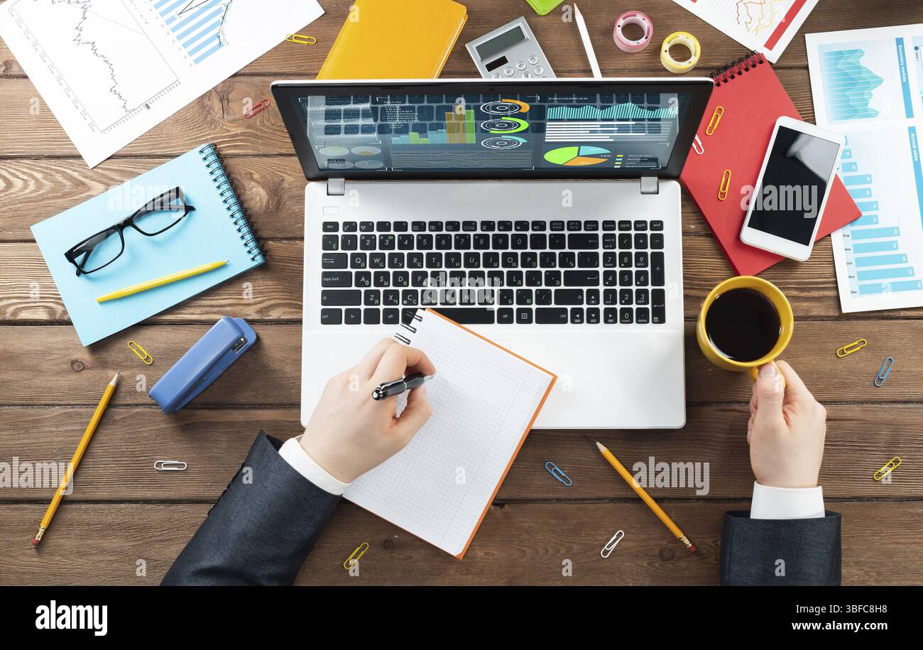 Gros plan des mains d'homme d'affaires travaillant à l'ordinateur portable. Bureau vue de dessus avec ordinateur et documents financiers sur table en bois. Profession commerciale des Banque D'Images