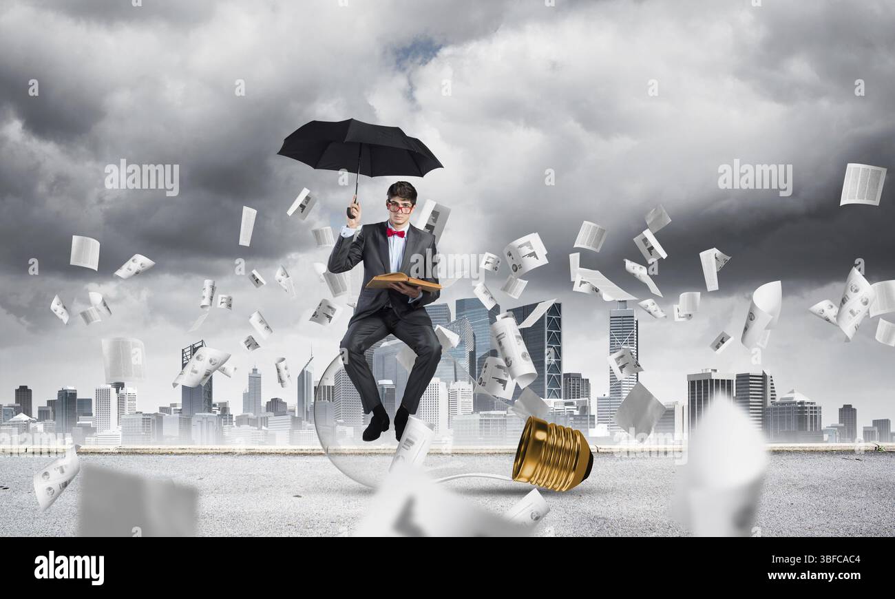 Jeune homme d'affaires avec parapluie et livre, autour voler dans des documents de chaos Banque D'Images