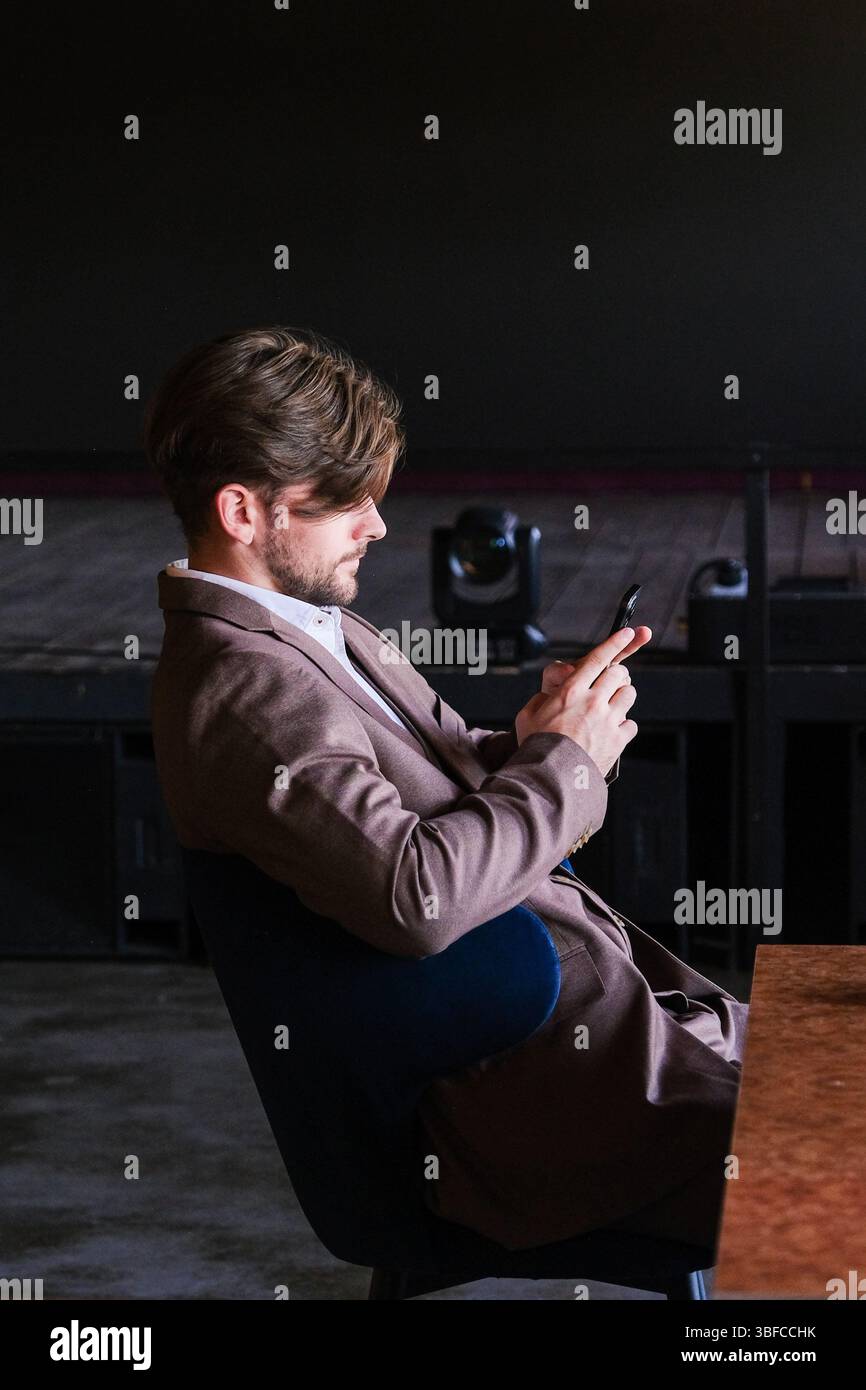 moscou, russie, 22.05.2025 Un homme en costume est assis à une table et regarde son téléphone portable. Concept de modernité et de technologie, comme l'homme est usi Banque D'Images