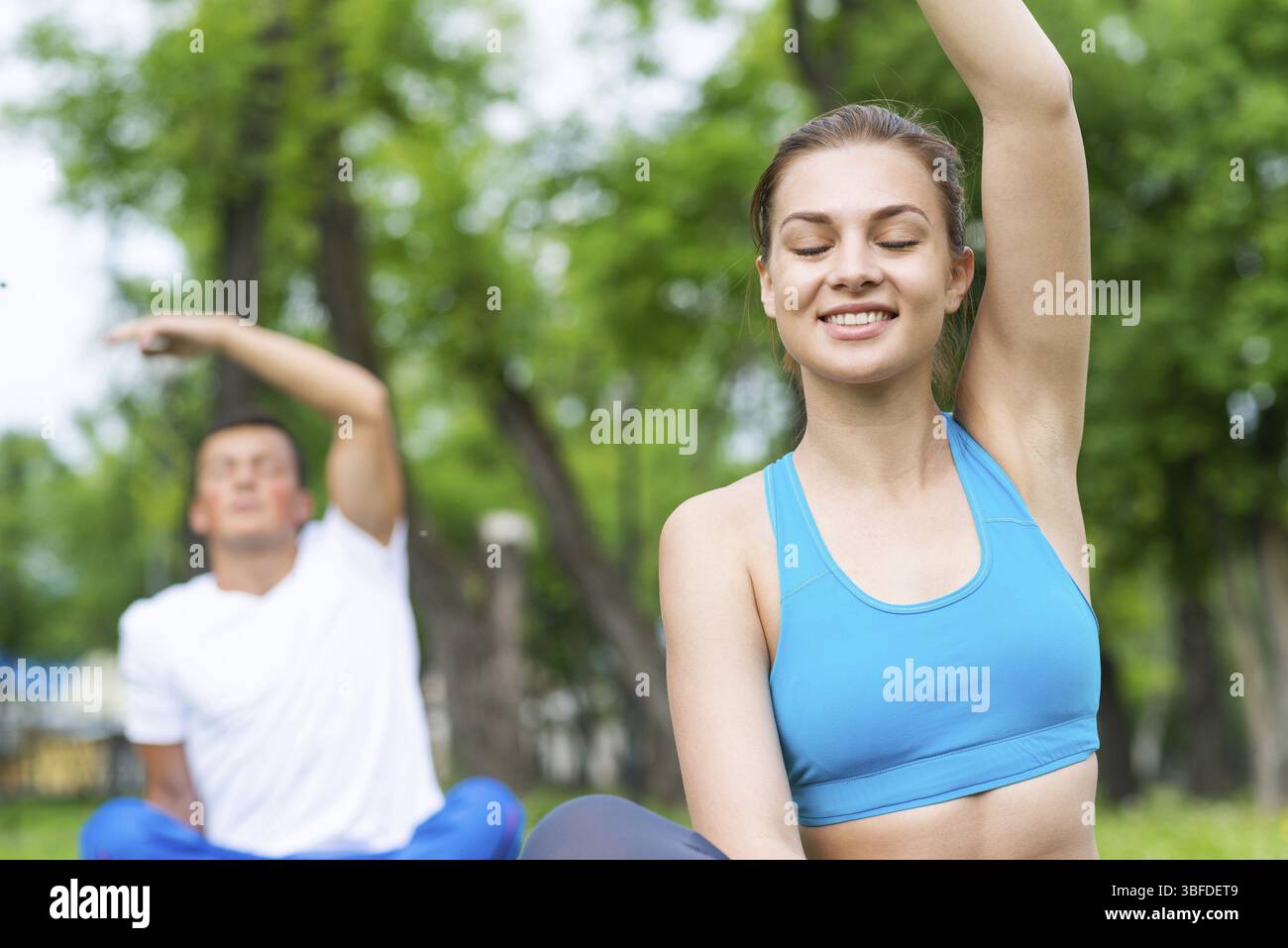 Jeune couple faisant du yoga dans le parc ensemble. Homme et femme assis dans le yoga pose sur l'herbe verte. Entraînement et méditation en cours de yoga en plein air au su ensoleillé Banque D'Images