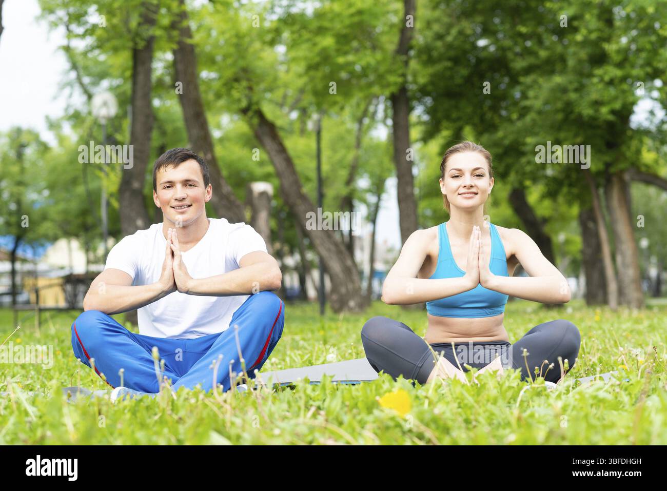 Jeune couple faisant du yoga dans le parc ensemble. Homme et femme assis dans le yoga pose sur l'herbe verte. Entraînement et méditation en cours de yoga en plein air au su ensoleillé Banque D'Images