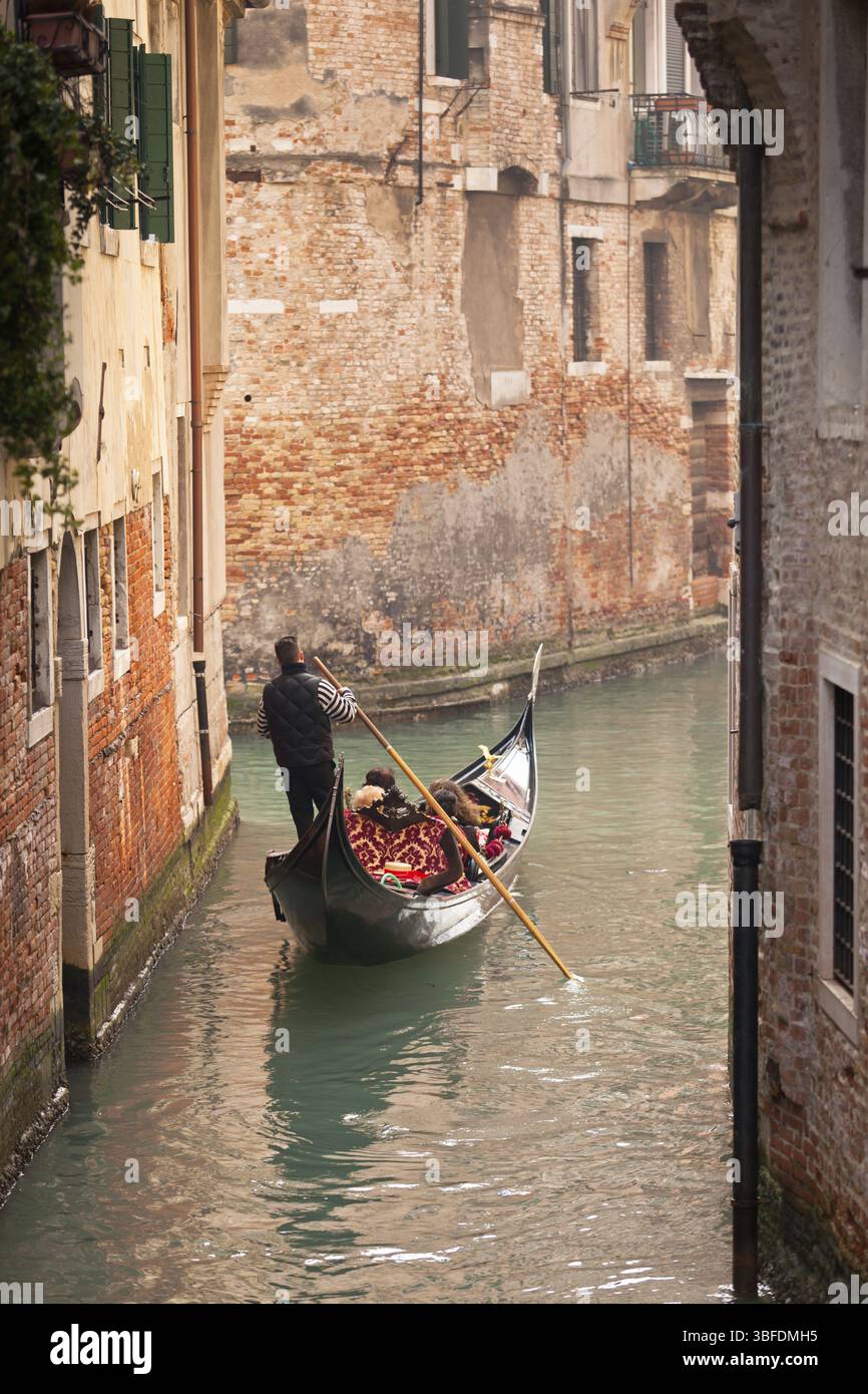 Une gondole avec des touristes descendant un petit canal bordé de maisons urbaines Banque D'Images