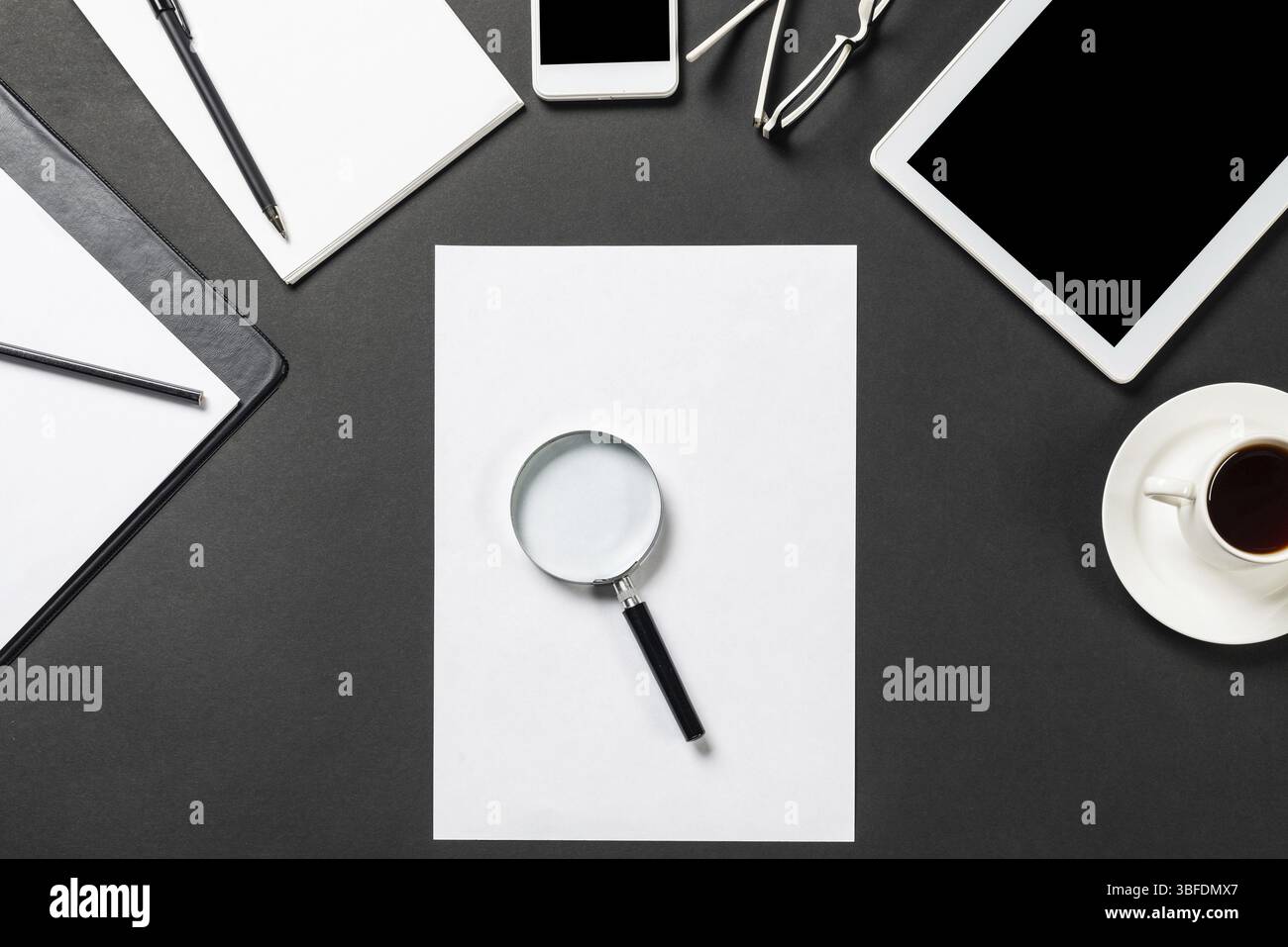 Vue de dessus du lieu de travail moderne avec feuille de papier vierge. Surface noire plate avec smartphone, bloc-notes et tasse de café. Vue de dessus de l'espace de travail de bureau et Banque D'Images