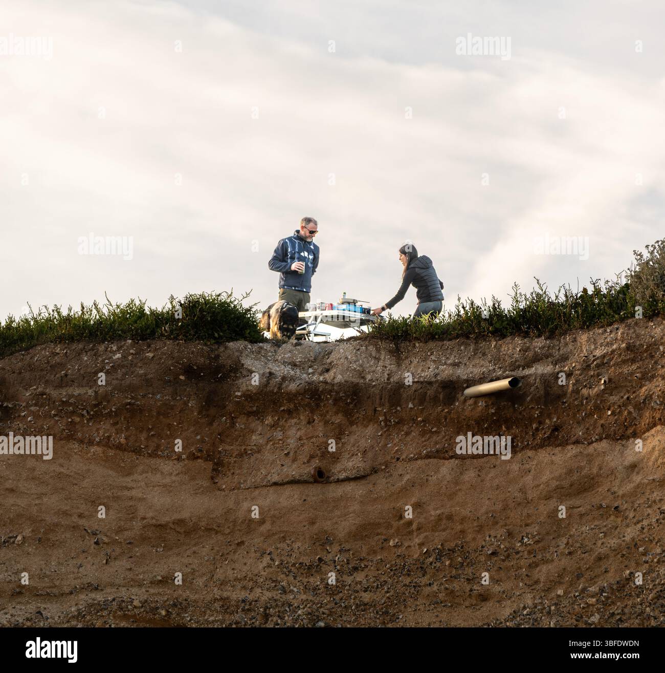 Un couple, accompagné d’un chien berger allemand, a installé une table et des chaises précaires près du bord de la falaise à Birling Gap pour prendre un repas Banque D'Images