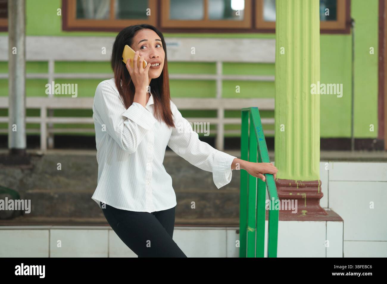 Femme indonésienne confiante debout dans les escaliers, parlant sur un téléphone portable. Banque D'Images