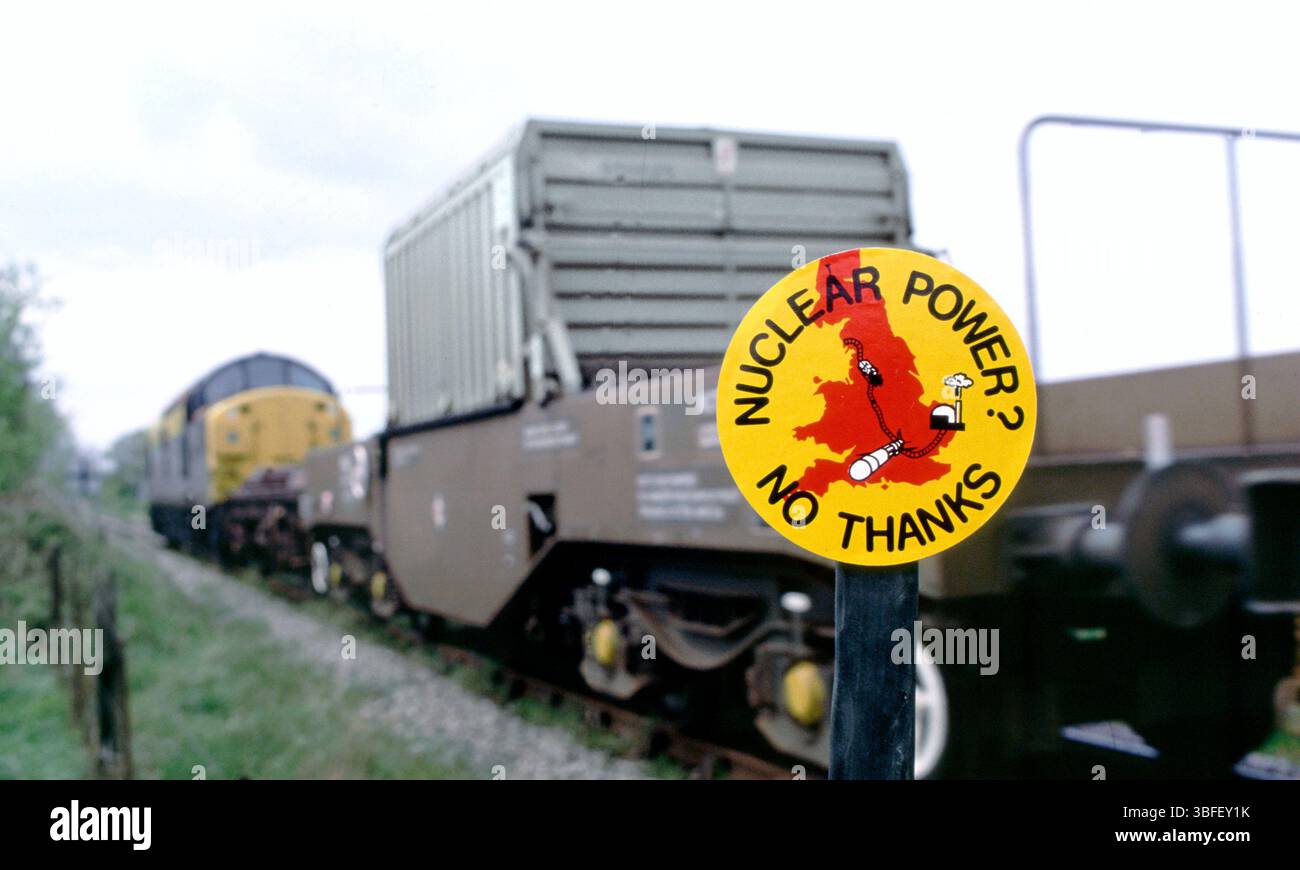 Un train transportant une fiole de combustible nucléaire irradié de la centrale nucléaire de Sizewell à Sellafield dans le Cumbria passe un panneau anti-nucléaire sur un poteau près de la ligne de chemin de fer près de Leiston, Suffolk. Photo prise dans les années 1980 Banque D'Images