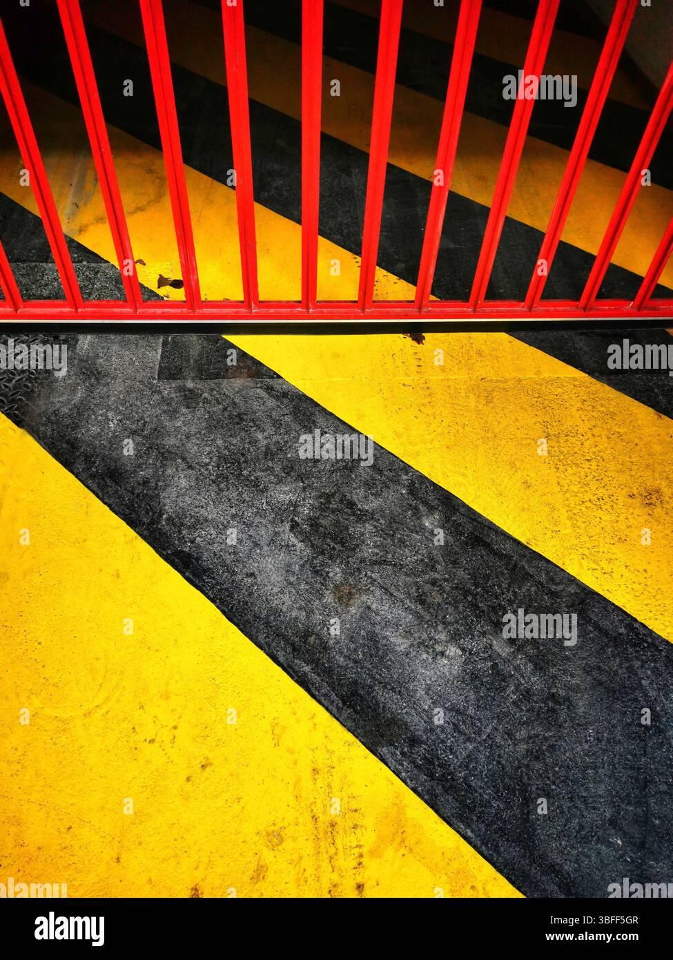 Des bandes jaunes vives et noires se croisent avec une barrière rouge vif sur une surface de béton. Entrée du parking Banque D'Images