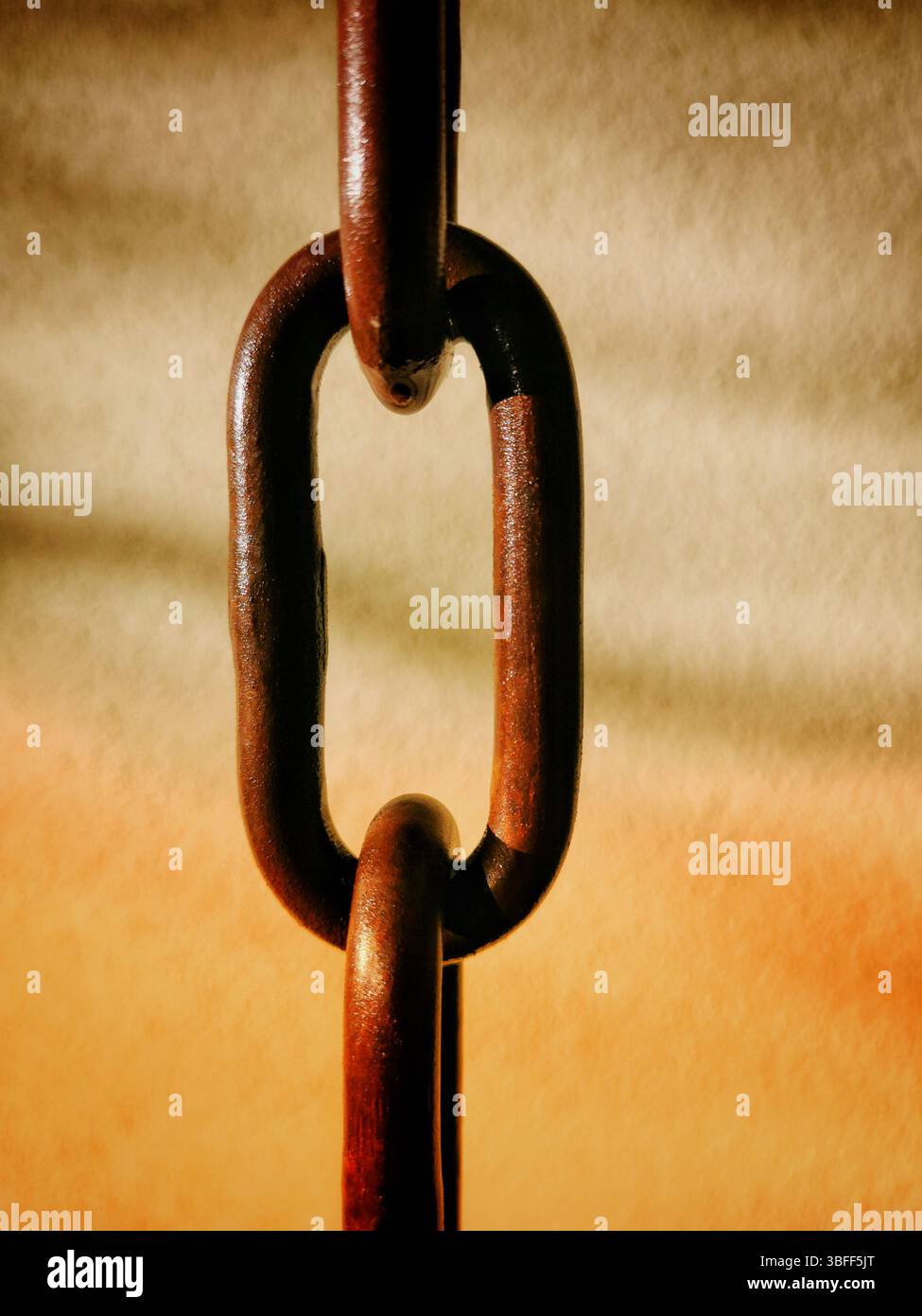 Gros plan d'une chaîne rouillée avec des maillons imbriqués suspendus sur un fond chaud légèrement flou. Banque D'Images