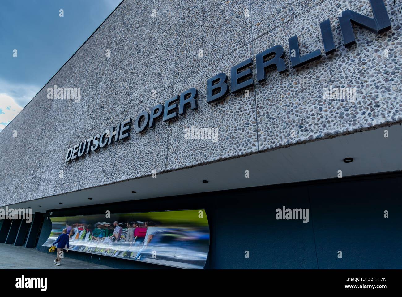 Extérieur contemporain de Deutsche Oper Berlin avec mur de pierre texturé et passant, capturé sous des nuages spectaculaires. Banque D'Images