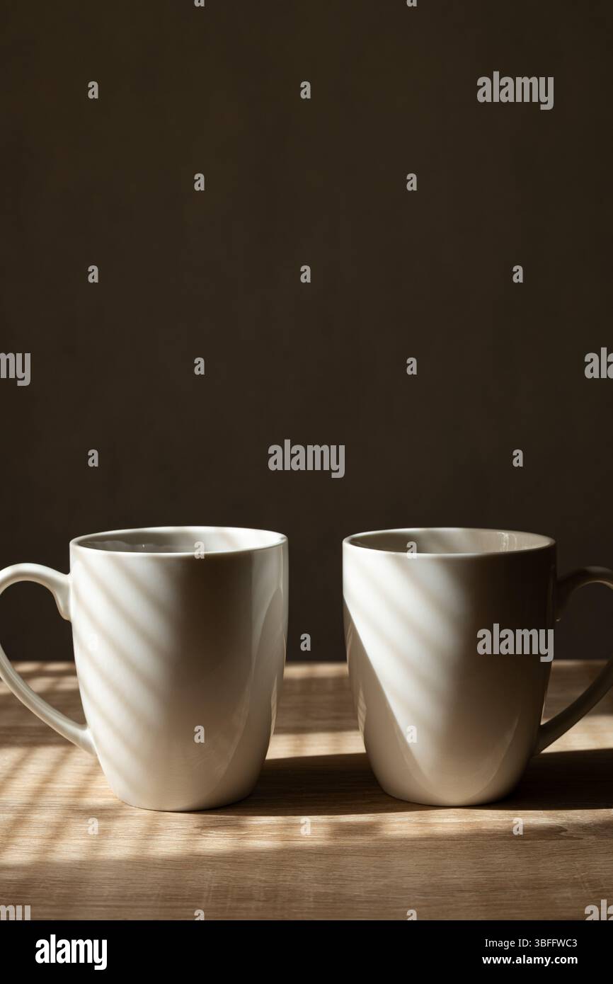 Deux tasses à café centrées dans le tiers inférieur avec éclairage latéral et ombres aveugles de fenêtre Banque D'Images Deux tasses à café centrées dans le tiers inférieur avec éclairage latéral et ombres aveugles de fenêtre Banque D'Images